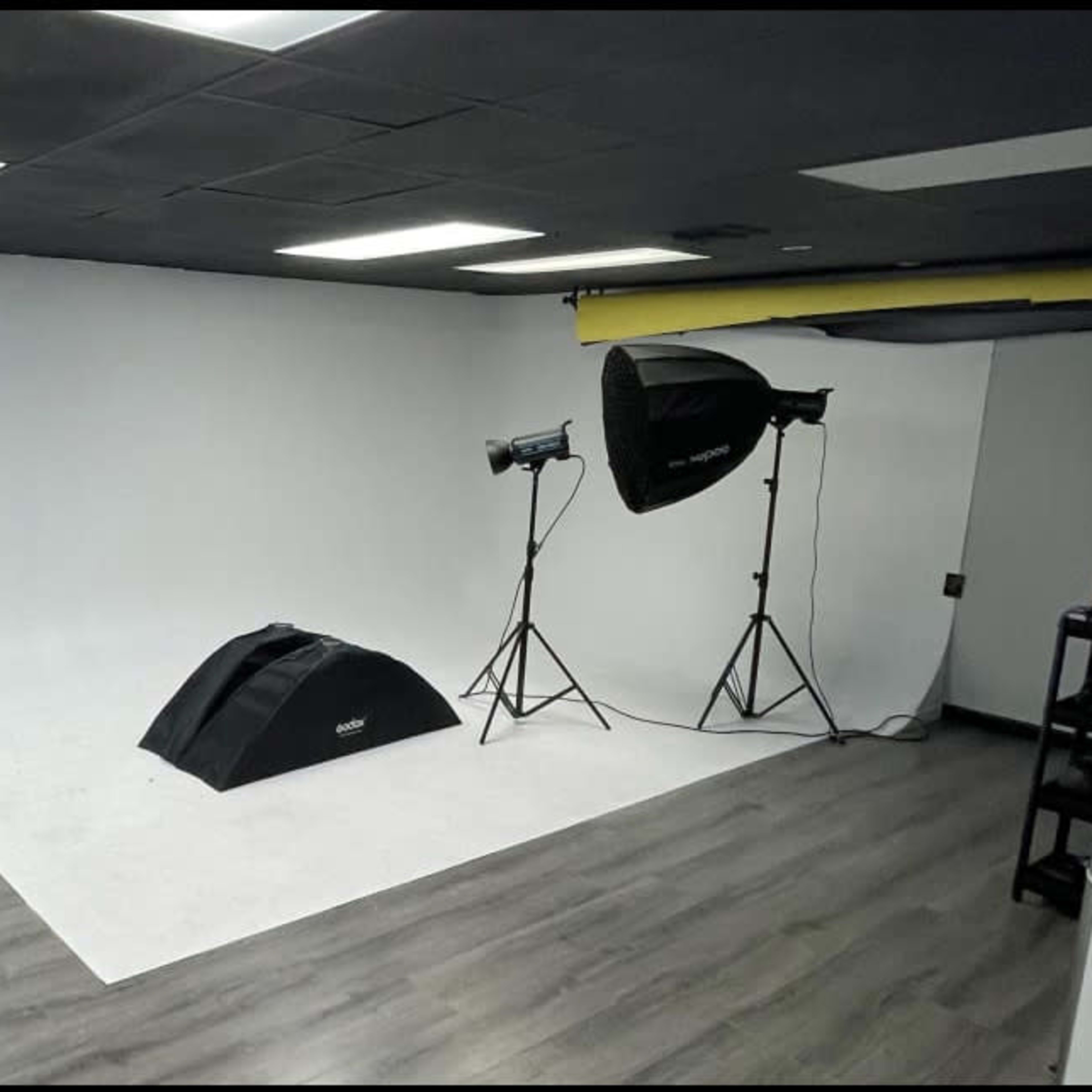 A photography studio with a white backdrop, studio lighting, and a stool against the wall.