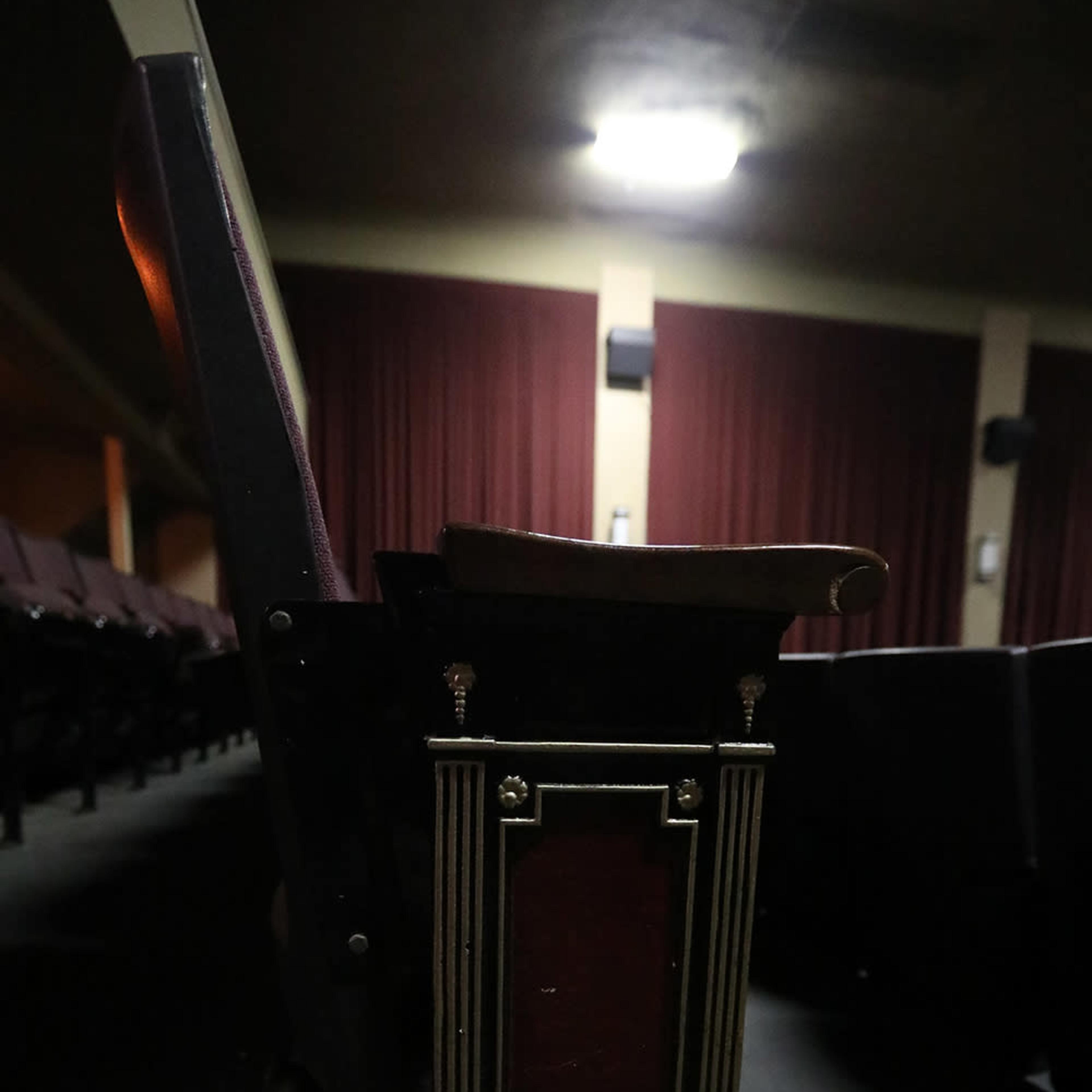 A wooden armrest table attached to a theater seat in a dimly lit auditorium.