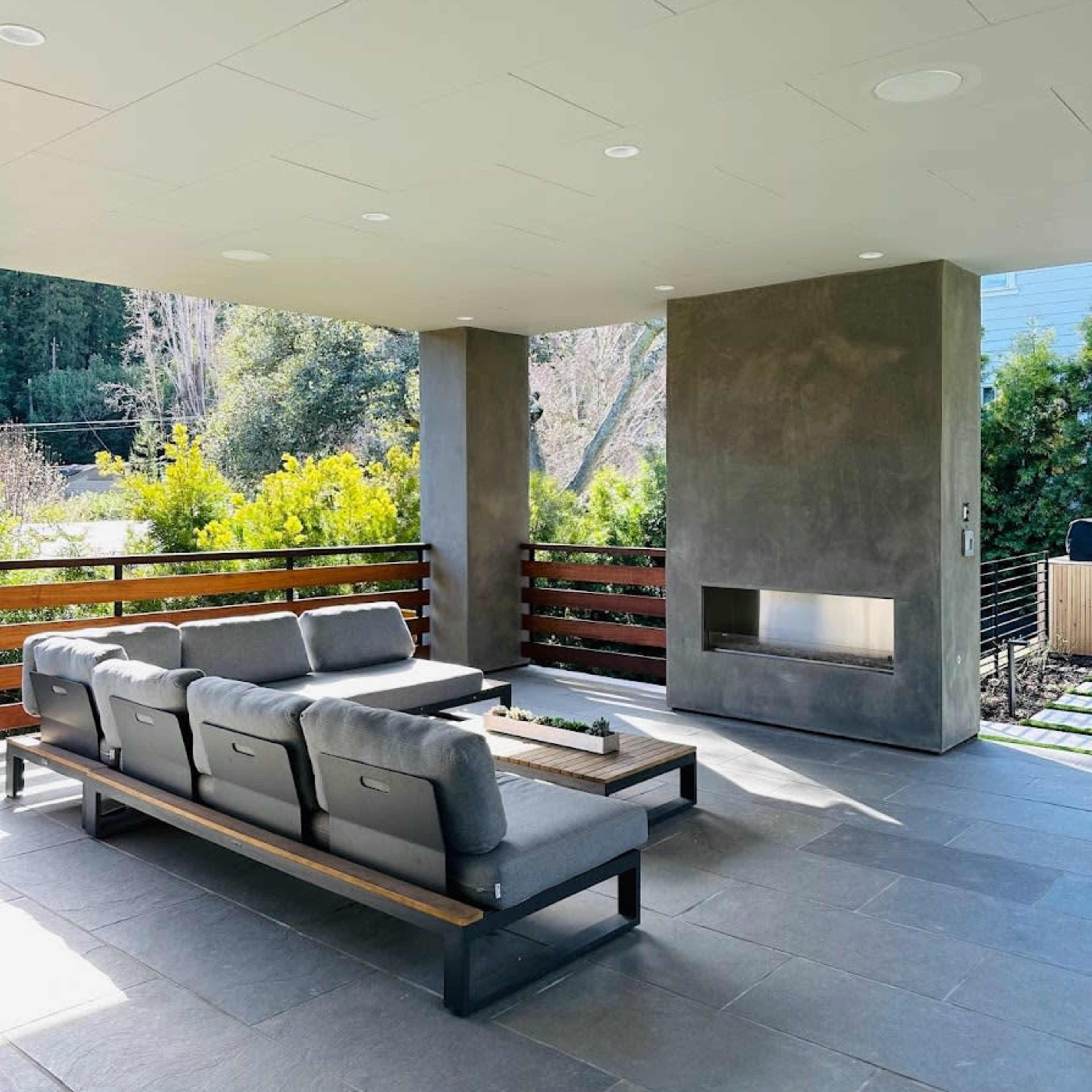A modern covered patio area featuring a sectional sofa and a built-in fireplace.