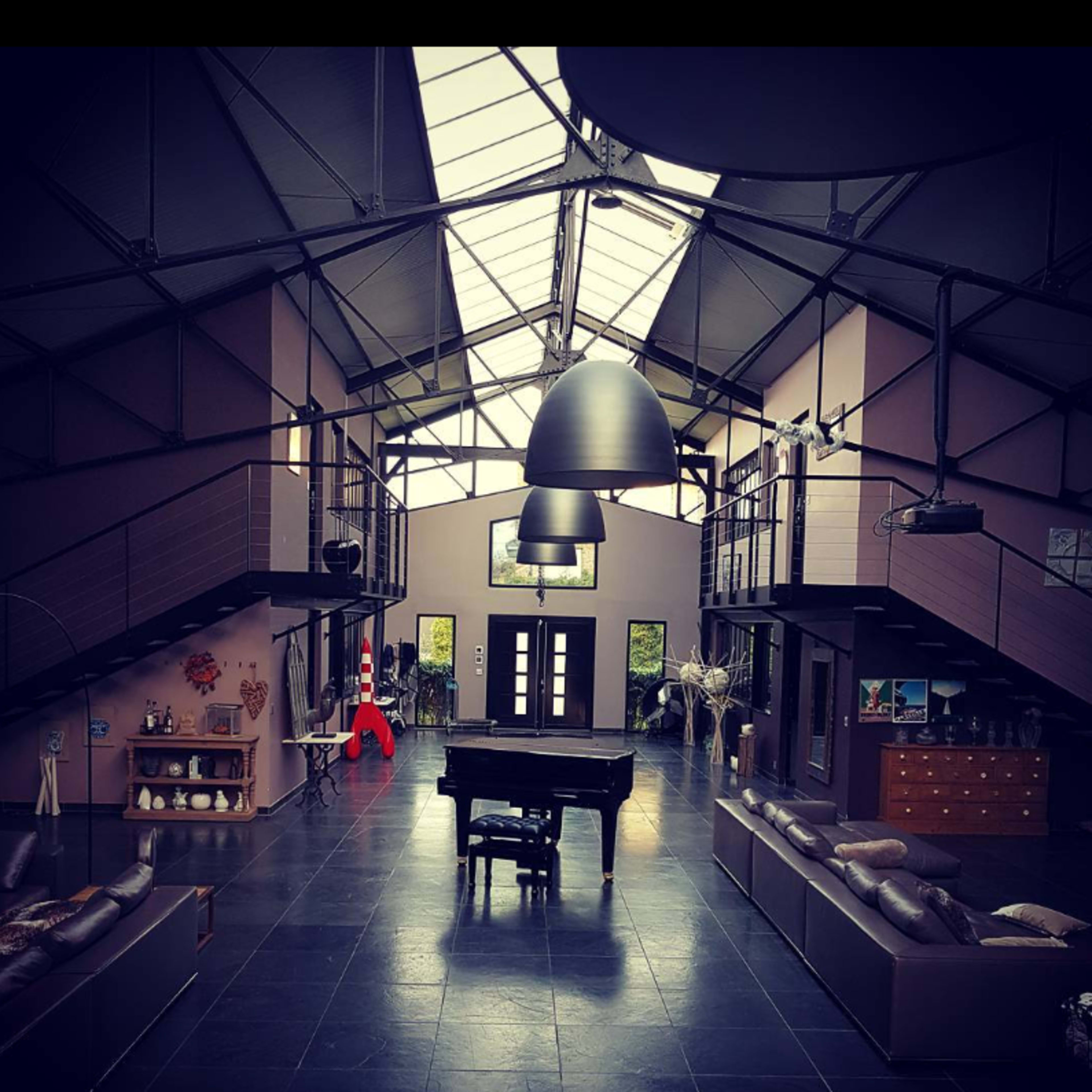 The interior of a spacious, modern loft with a grand piano at the center, large windows, and a high ceiling.