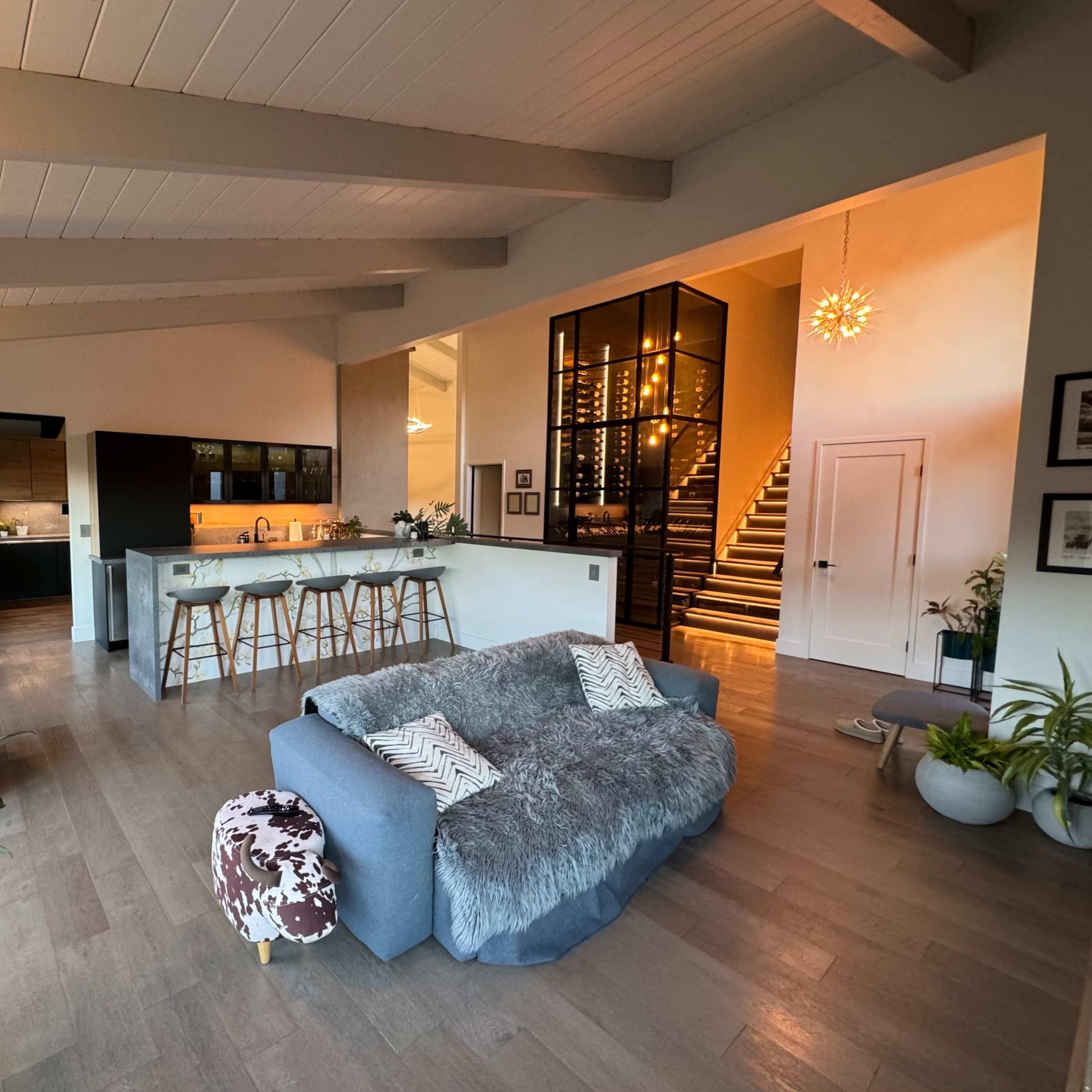 A modern, open-concept living space with a cozy gray sofa, a kitchen with bar seating, and a staircase leading to an upper level.