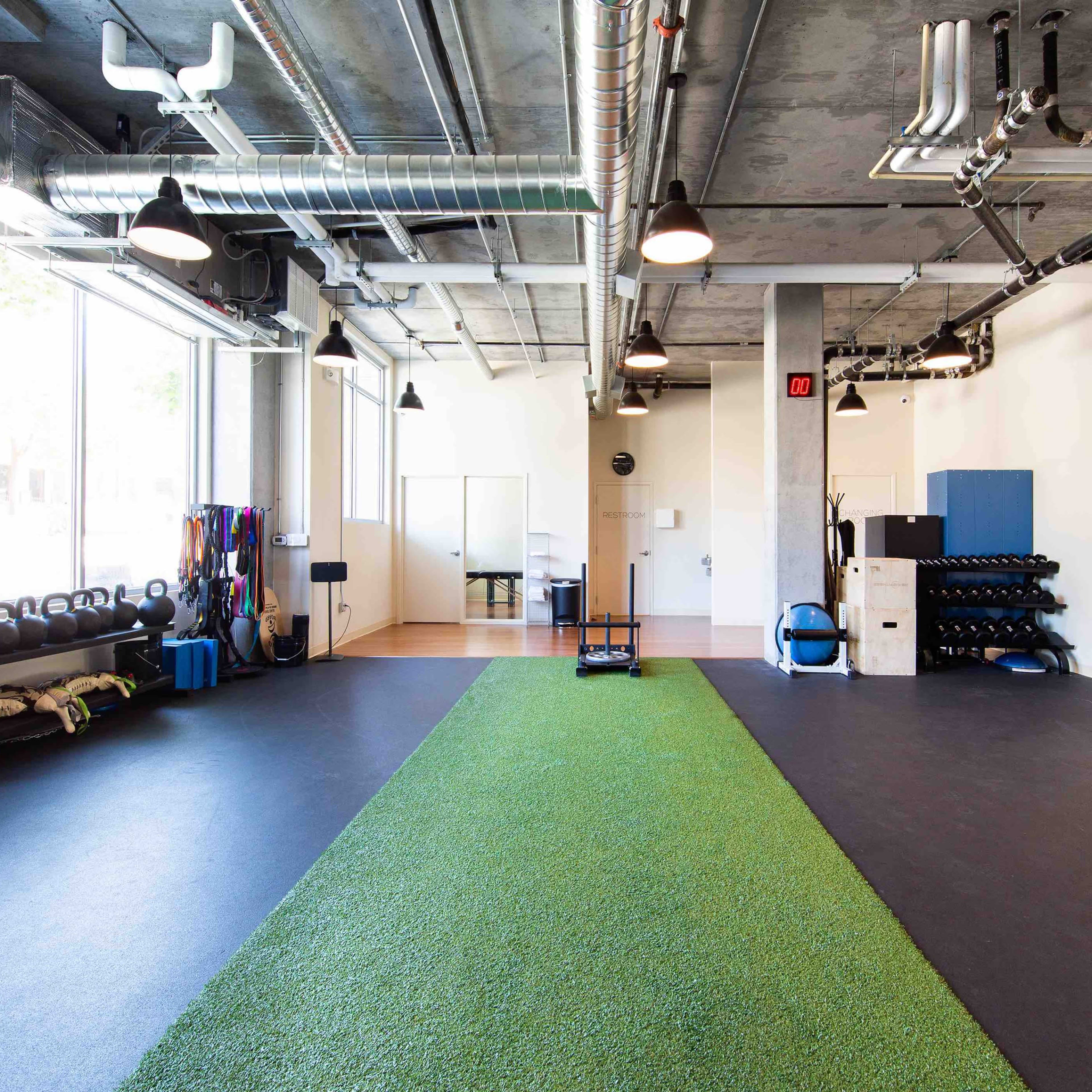 A modern gym space with artificial turf running down the center and various workout equipment arranged along the walls.