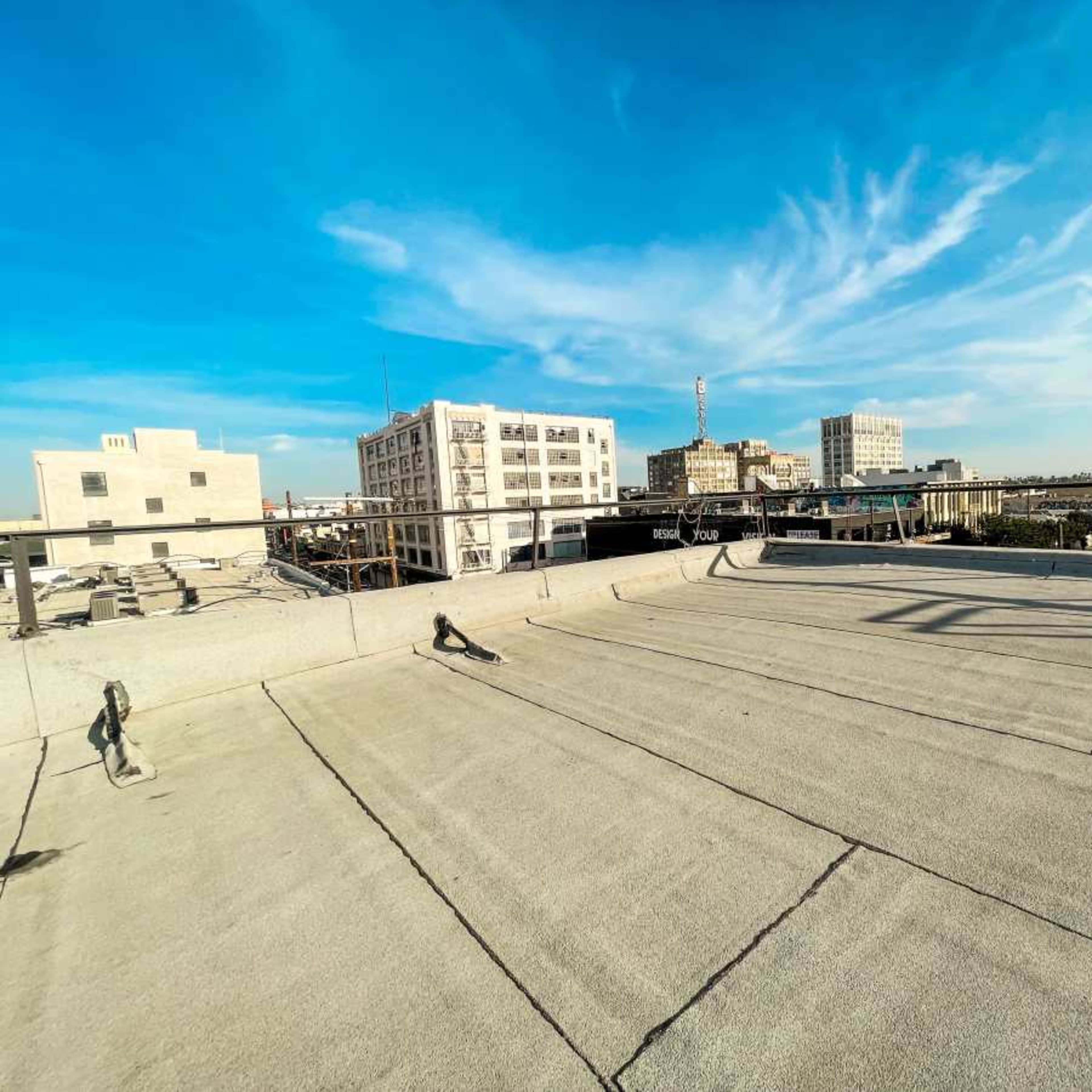 A flat rooftop overlooking a cityscape with several buildings and a clear blue sky in the background.