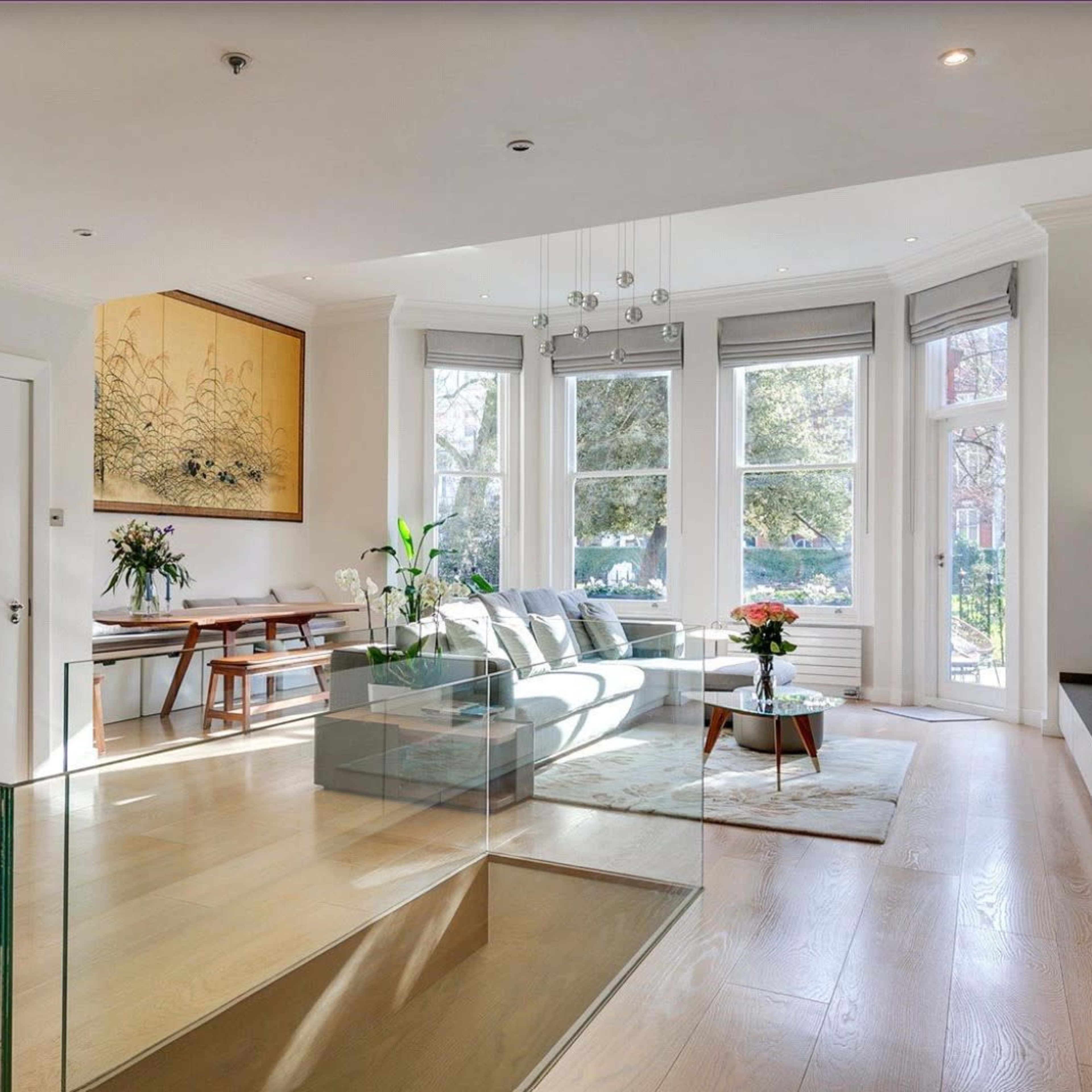 A bright, modern living room with a glass railing, contemporary furniture, and large windows allowing natural light to fill the space.