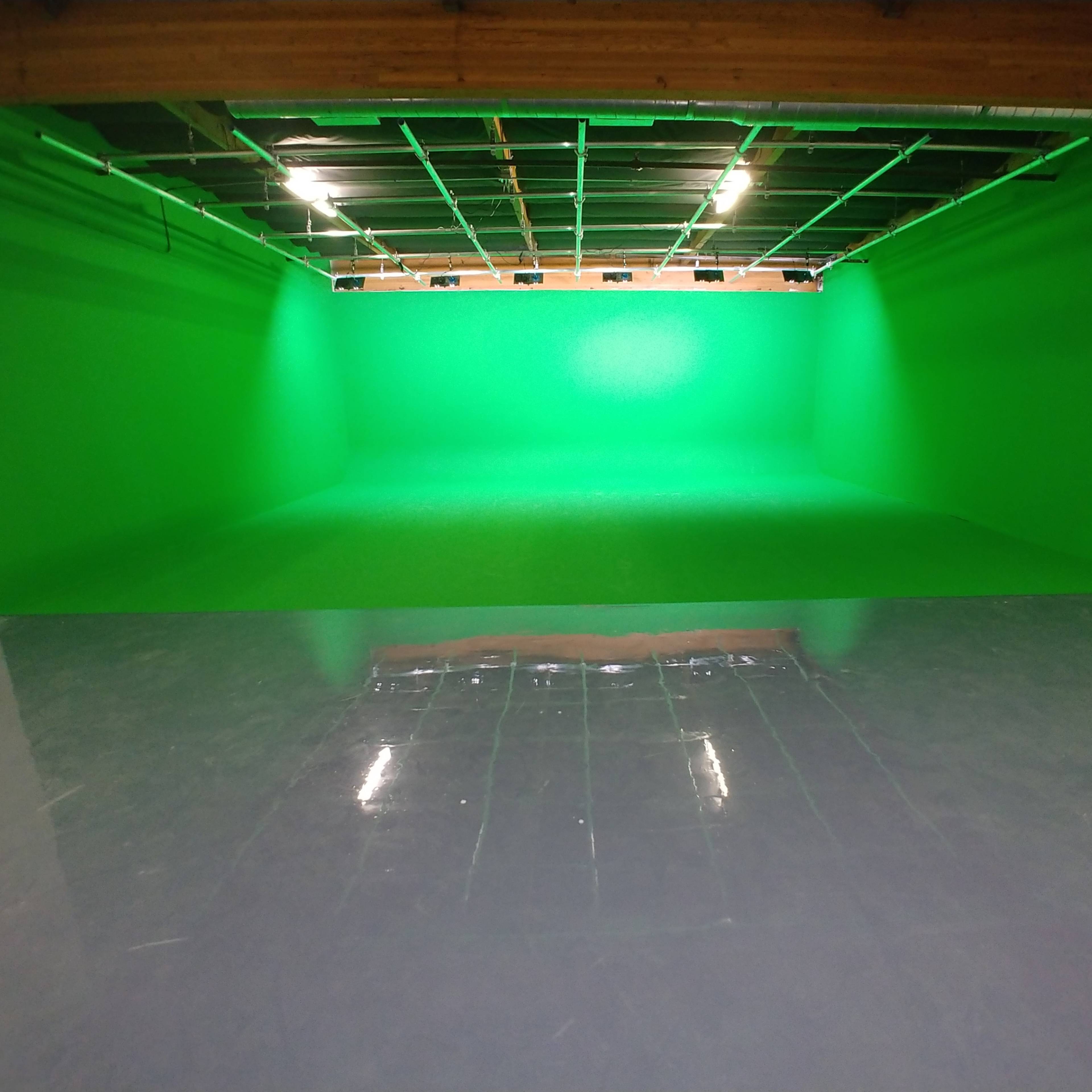 A spacious room with a bright green screen wall and a shiny gray floor.
