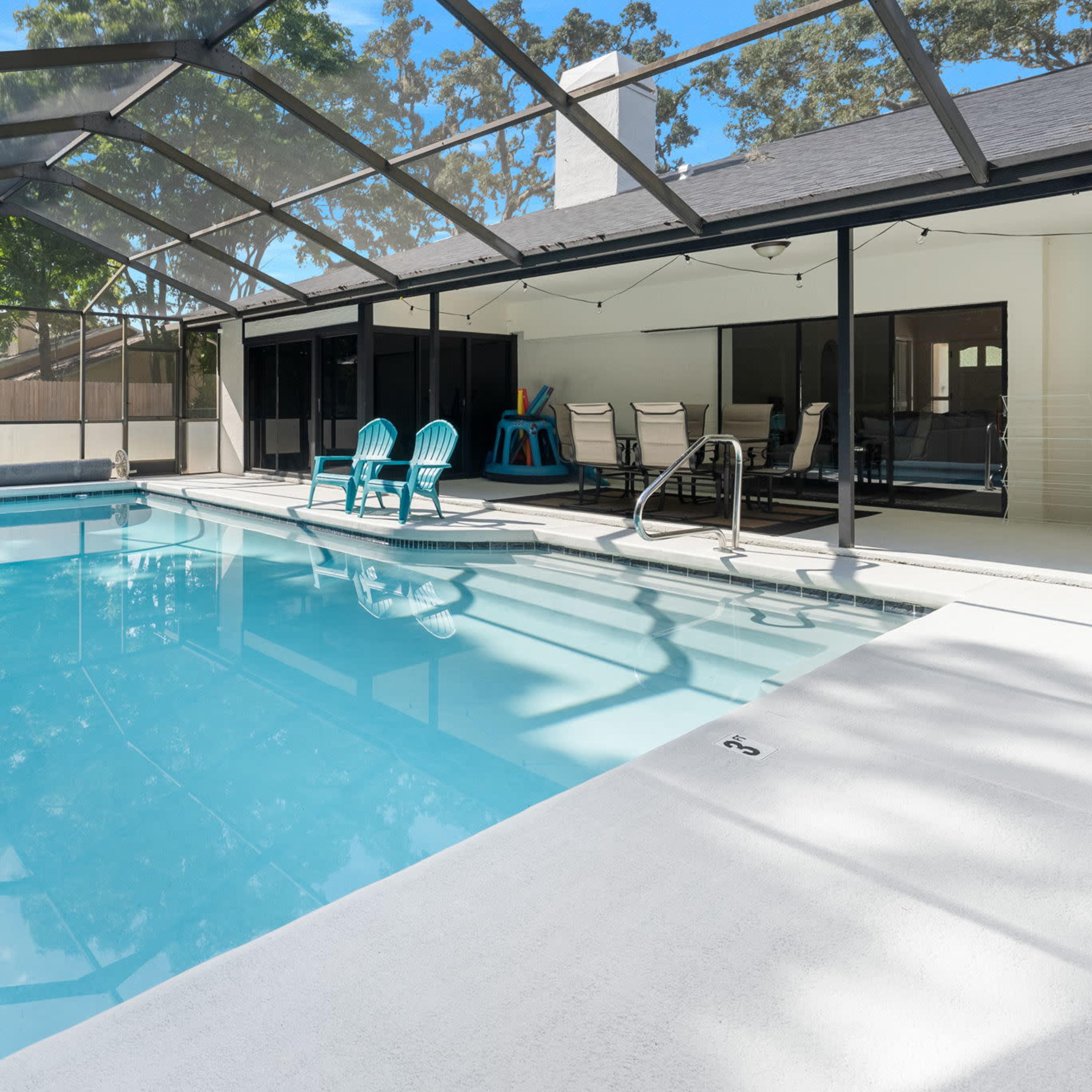 A clear swimming pool enclosed by a screened patio, flanked by lounge chairs and a covered seating area.