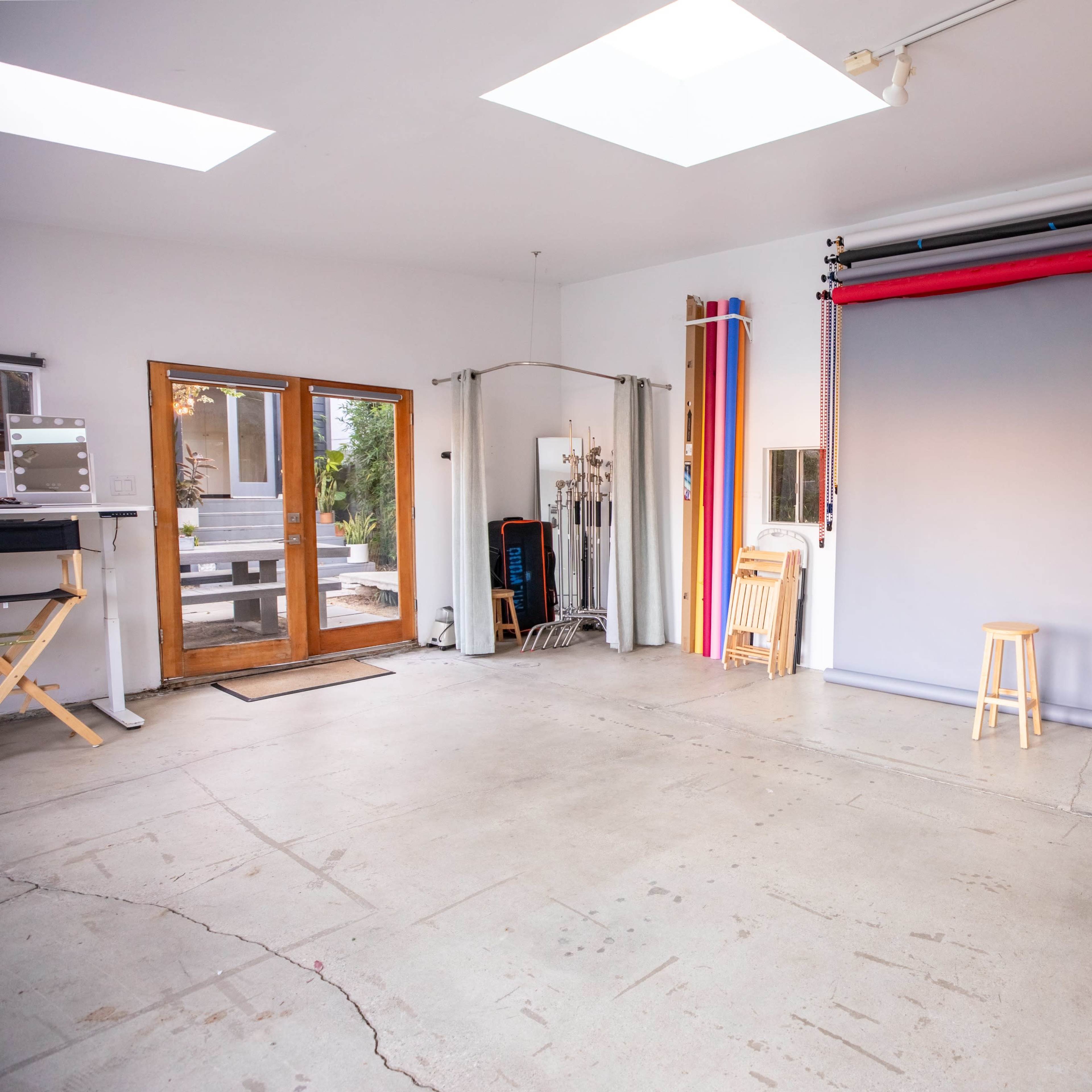 A spacious studio with a gray backdrop, a wooden stool in the center, and various photography equipment along the walls.