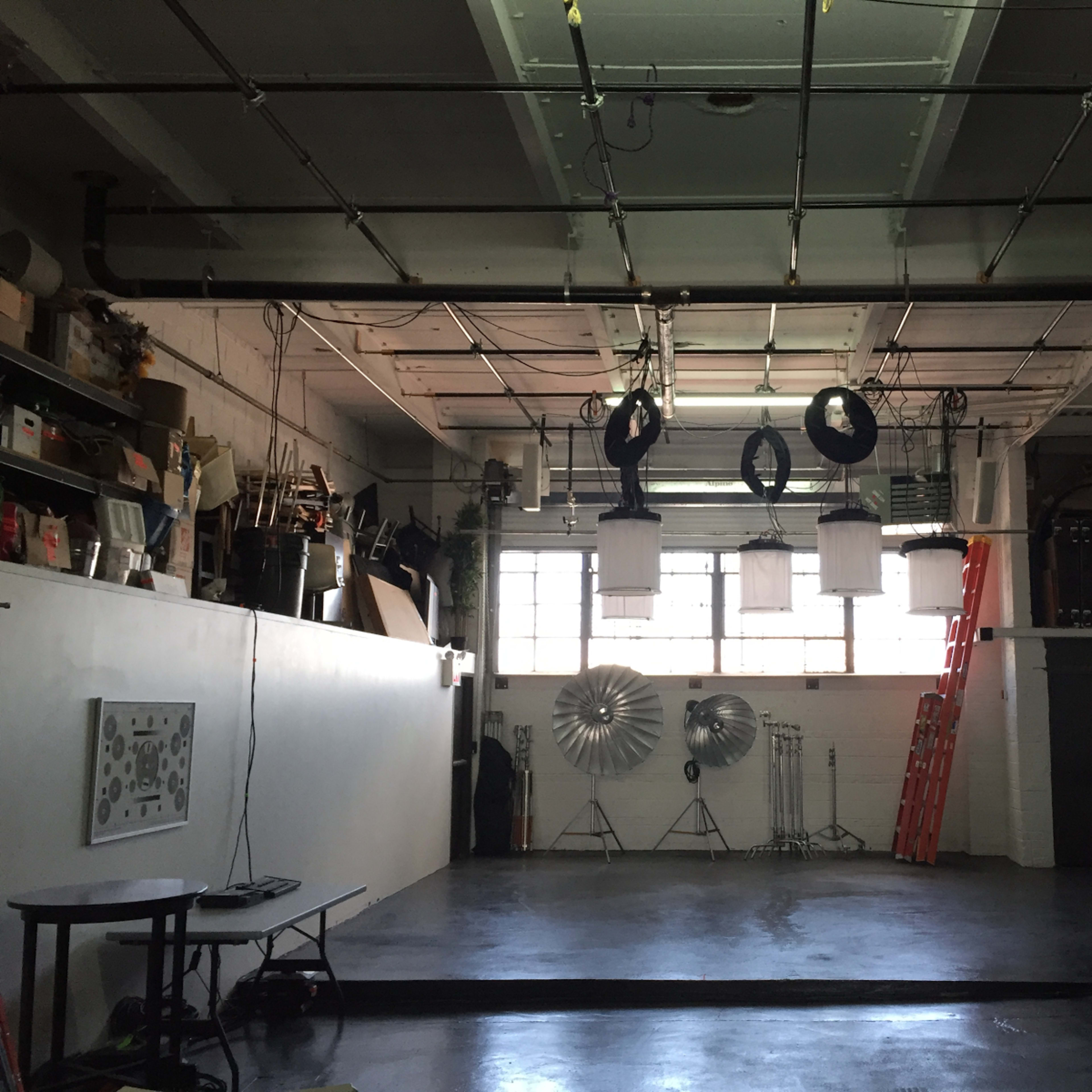 A spacious studio with large windows, various photography equipment, and a ladder against the wall.