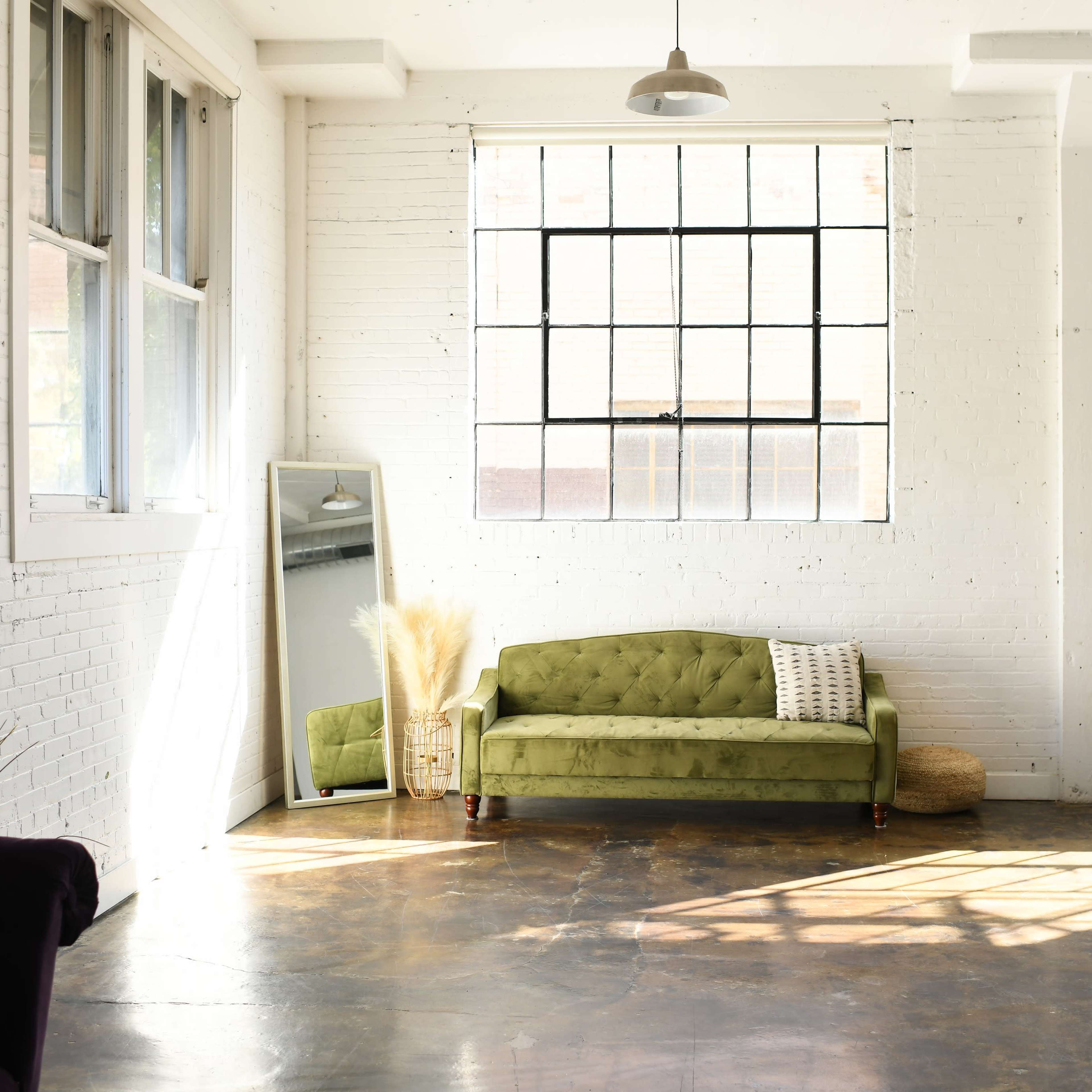A bright, spacious room featuring a green sofa, large windows, and minimal decor.