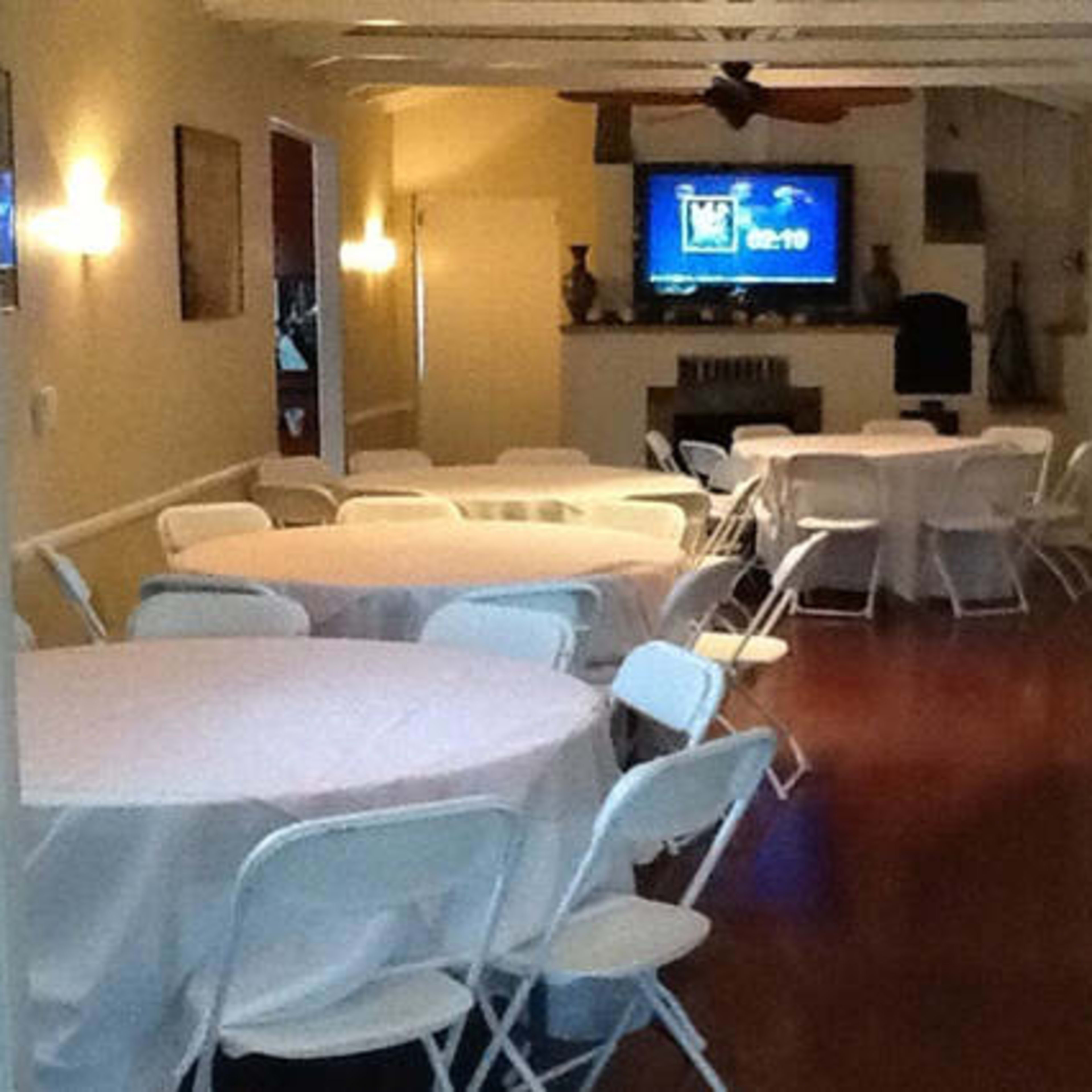 A banquet hall with several round tables set with white tablecloths and a large television screen at the end.