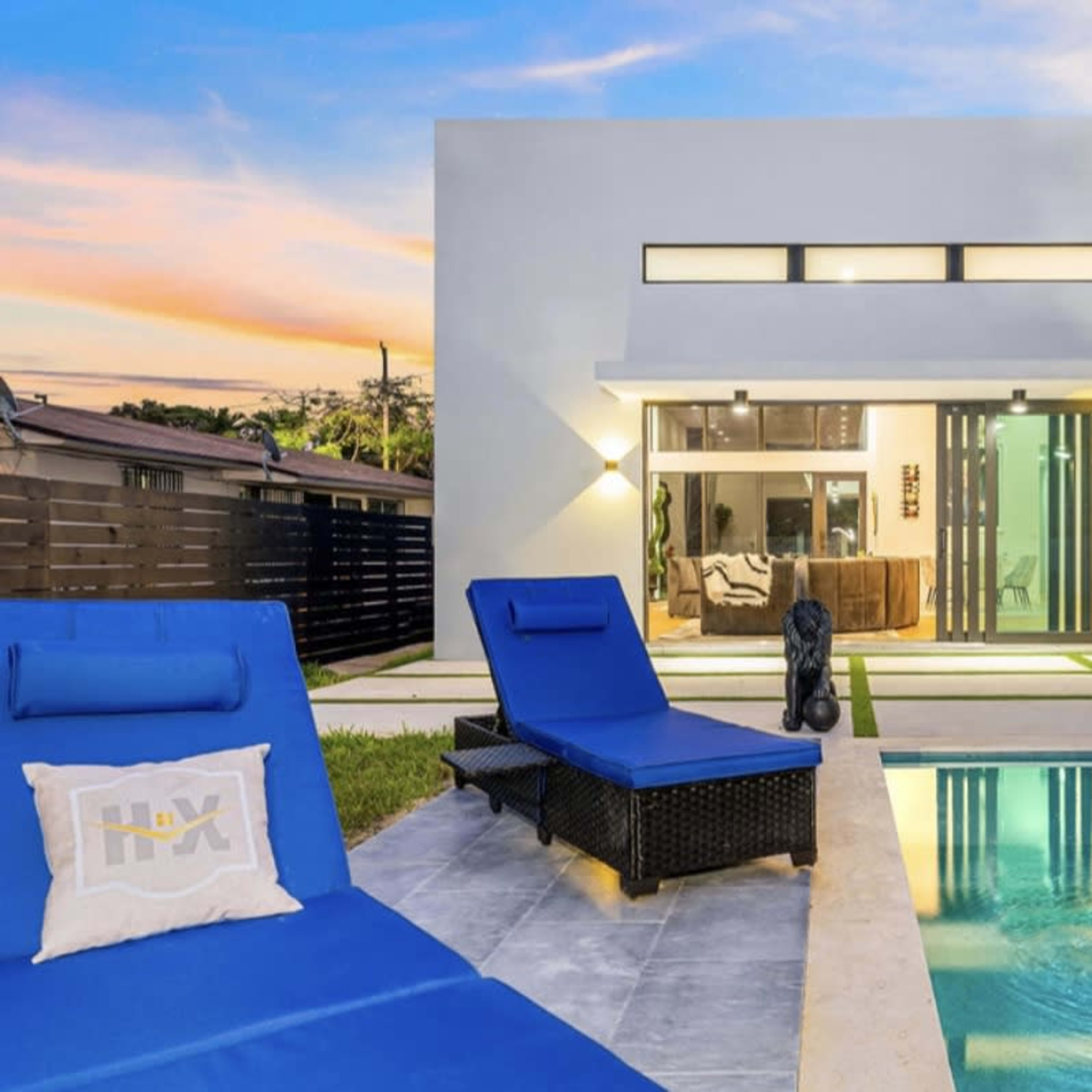 A modern house with large windows and a swimming pool is situated in a landscaped yard with lounge chairs.