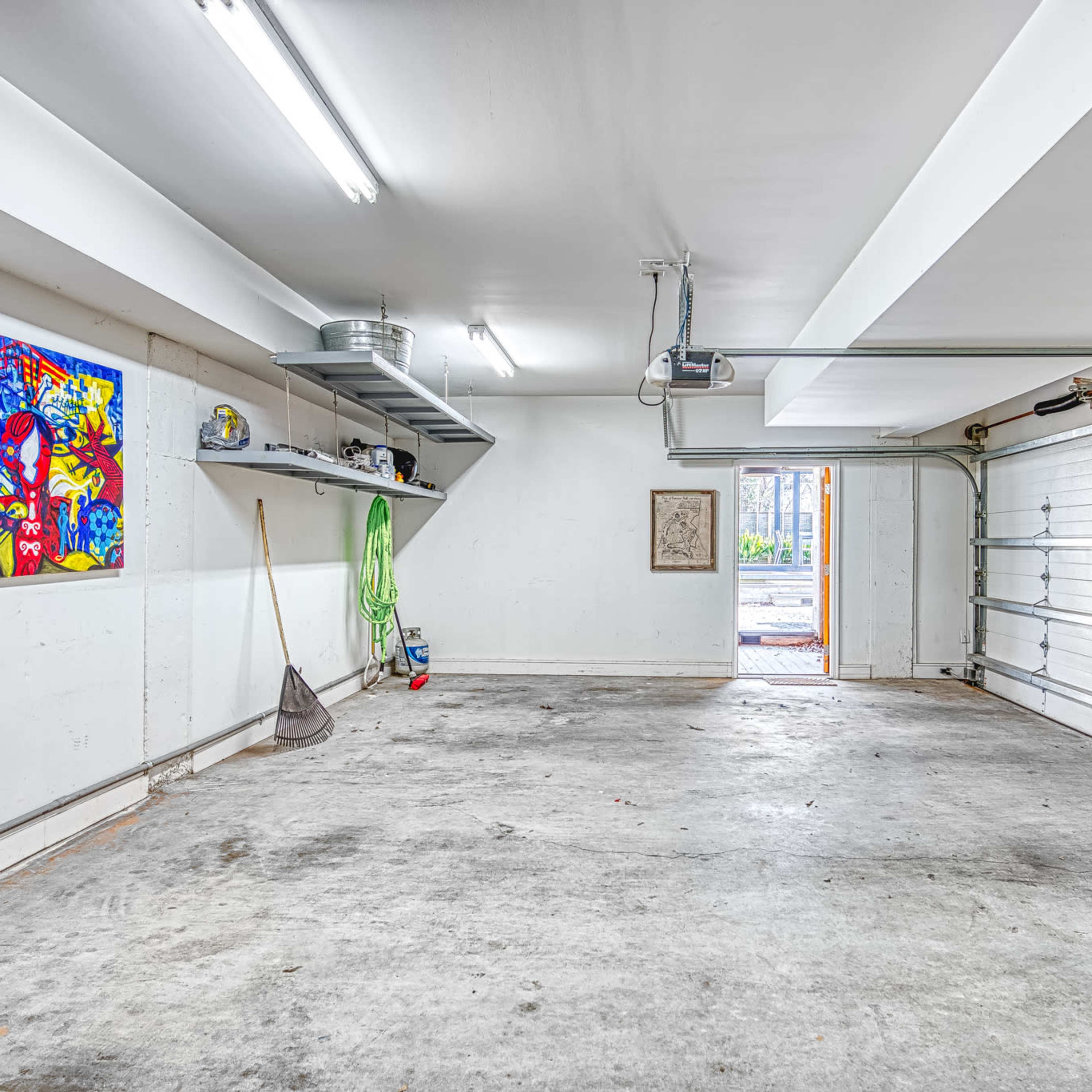 An empty garage with concrete flooring, a garage door on one side, and a colorful painting mounted on the wall.