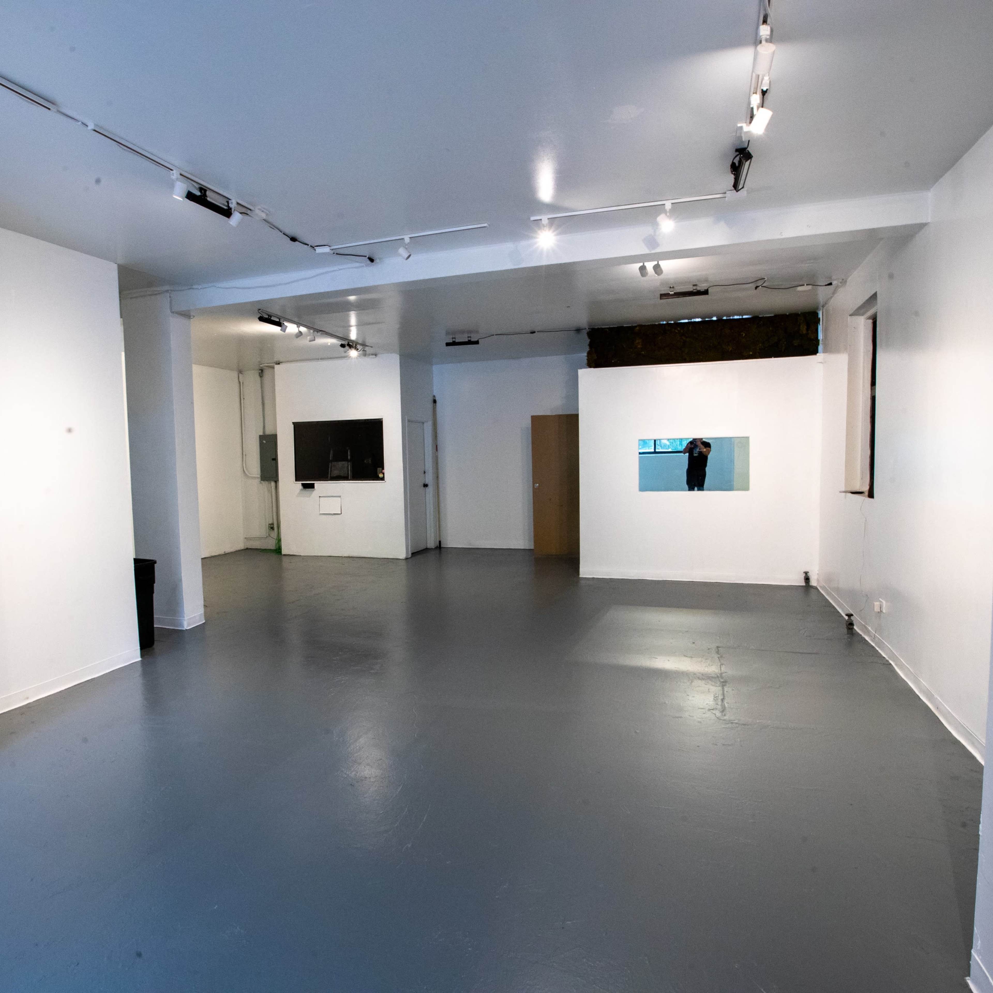 A spacious, empty room with white walls, gray flooring, and a few windows and doors.