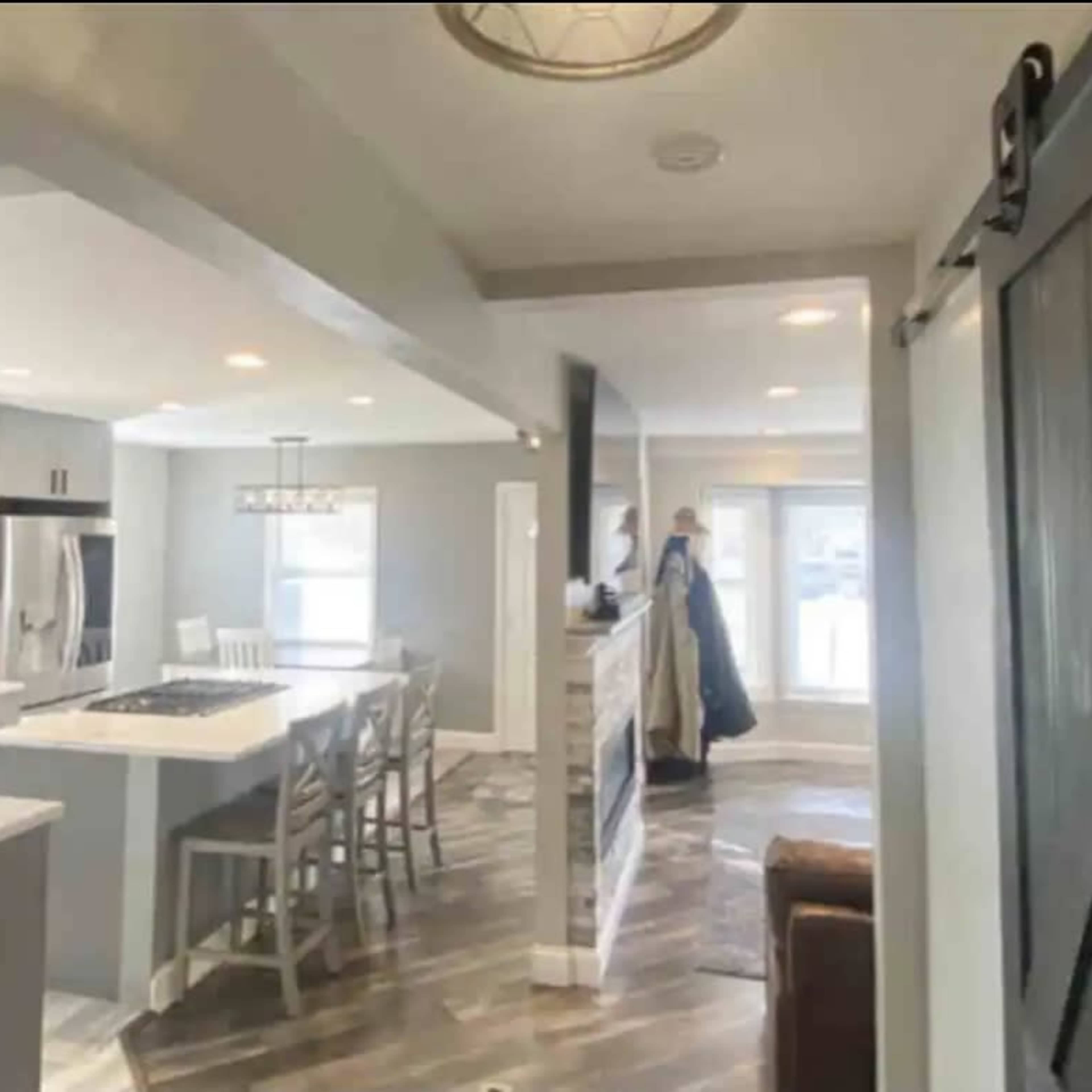 A modern kitchen and living area with a central island, dining space, and a sliding barn door leading to another room.
