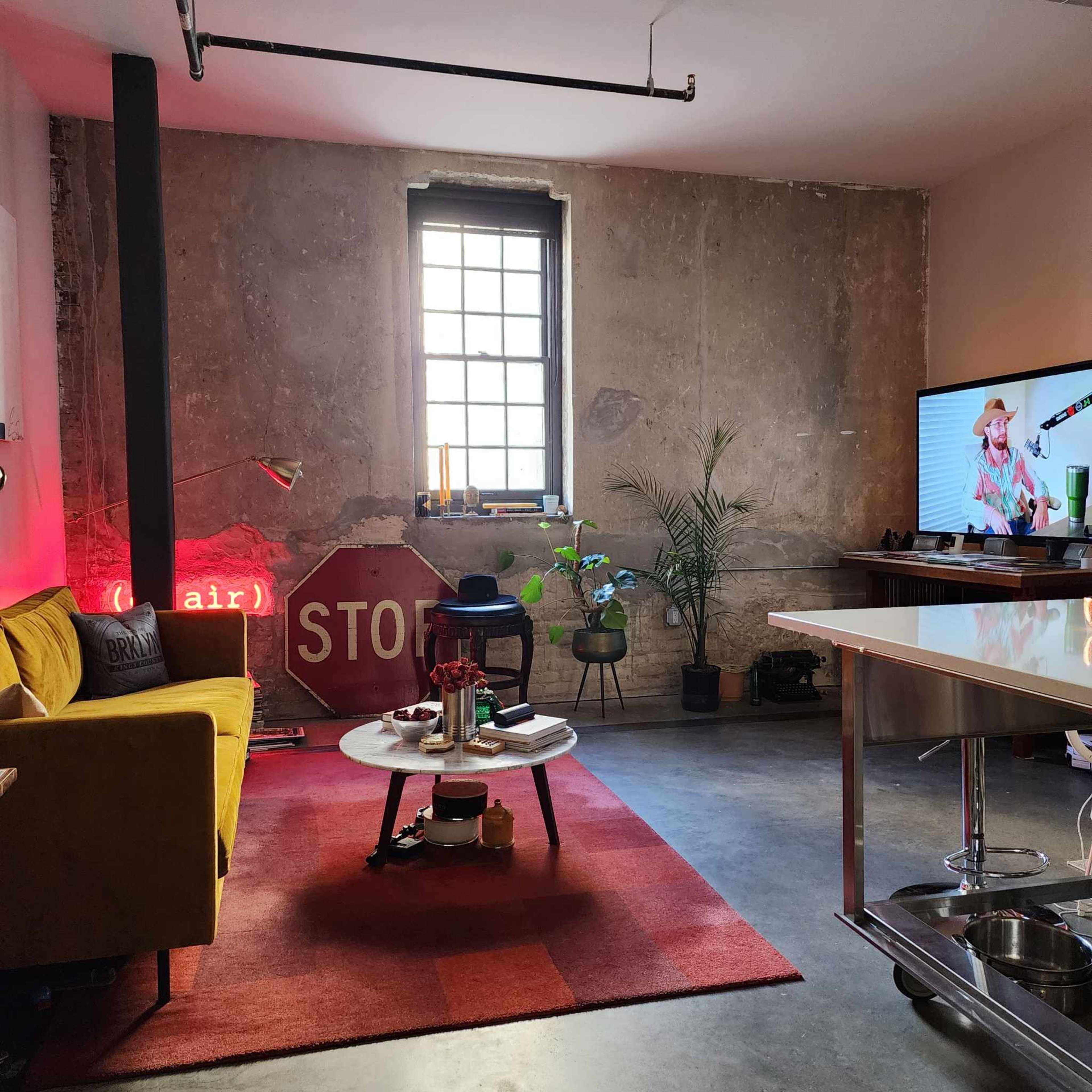 The scene features a modern living space with a yellow couch, a large red stop sign, a television displaying a woman wearing a hat, and a potted plant in a corner.