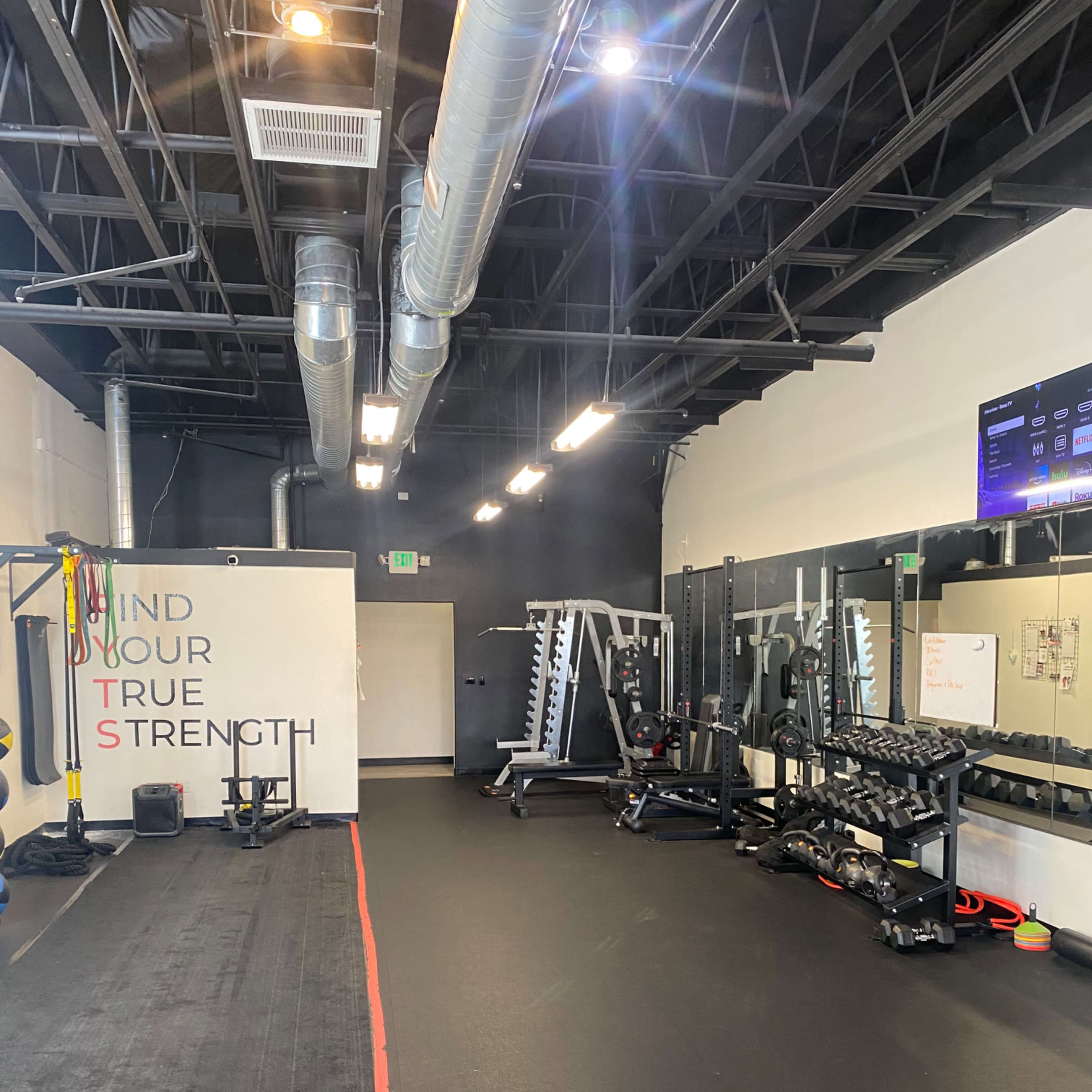A fitness gym with various exercise equipment, including weights and resistance bands, along with a motivational wall and mirrors.