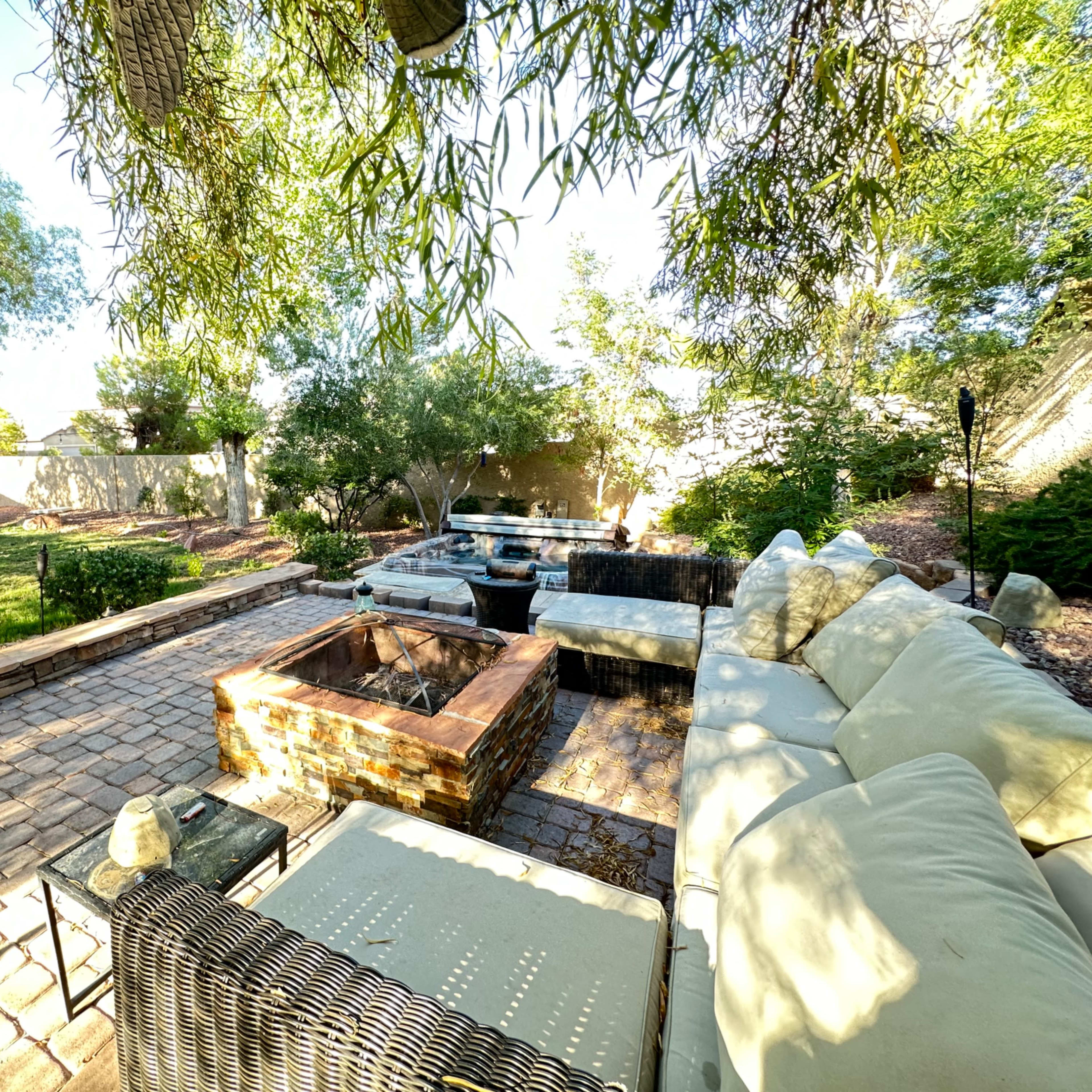 A backyard patio with a seating area, a fire pit, and surrounding greenery.