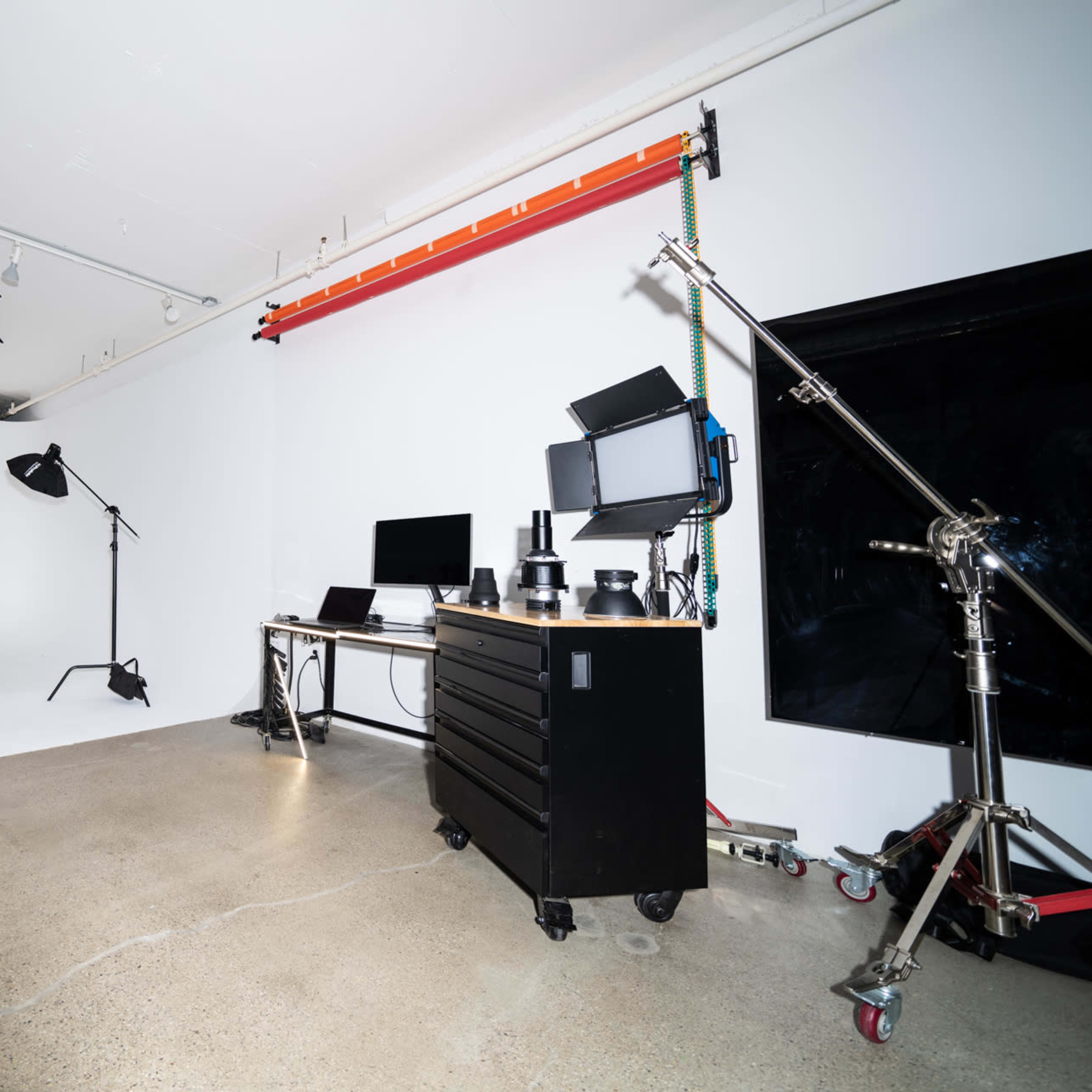 A photography studio with various lighting equipment, a computer setup, and a plain white backdrop.