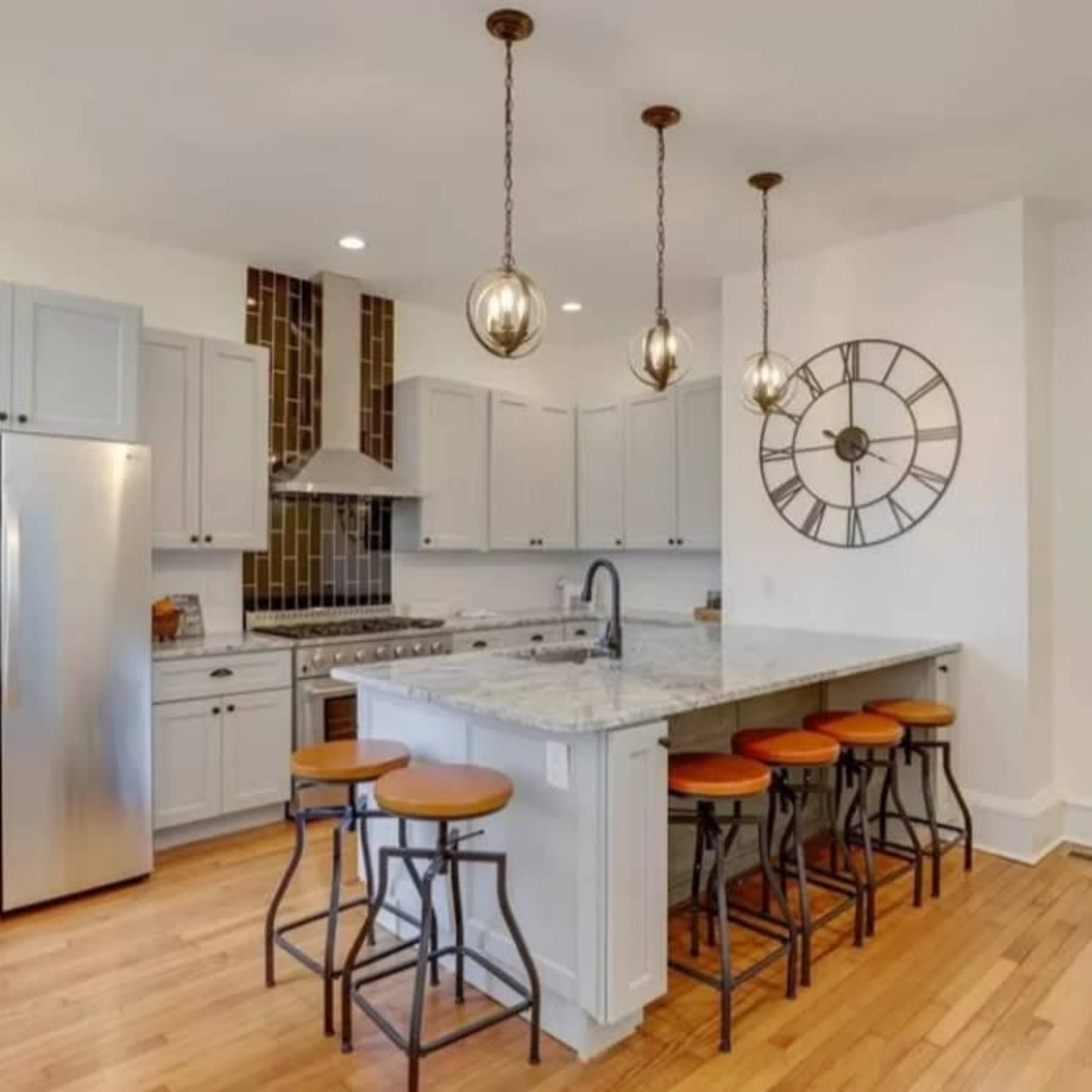 A modern kitchen featuring a large island with seating, stainless steel appliances, and pendant lighting above.