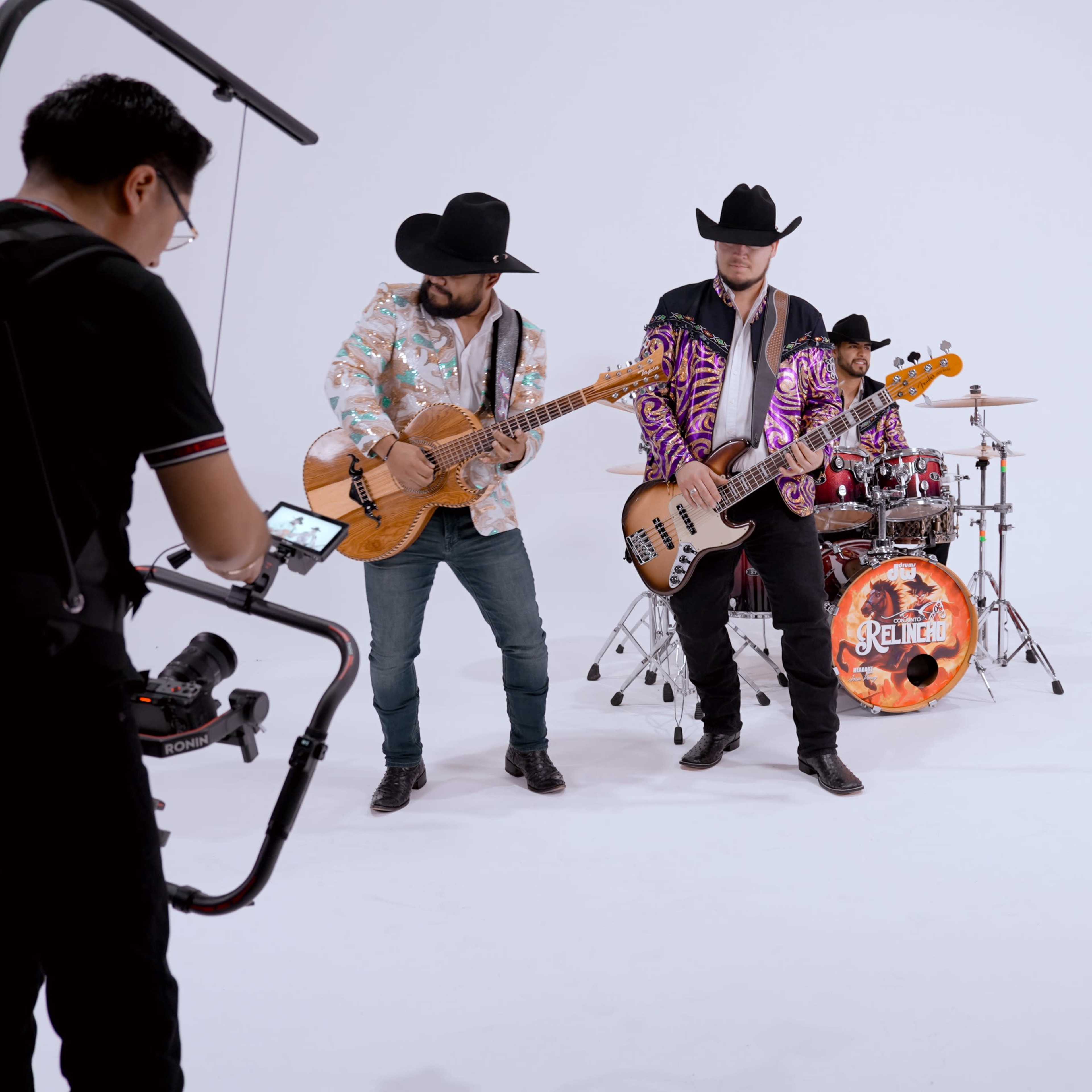 A band wearing matching outfits performs in a studio with a guitarist, bassist, and drummer.