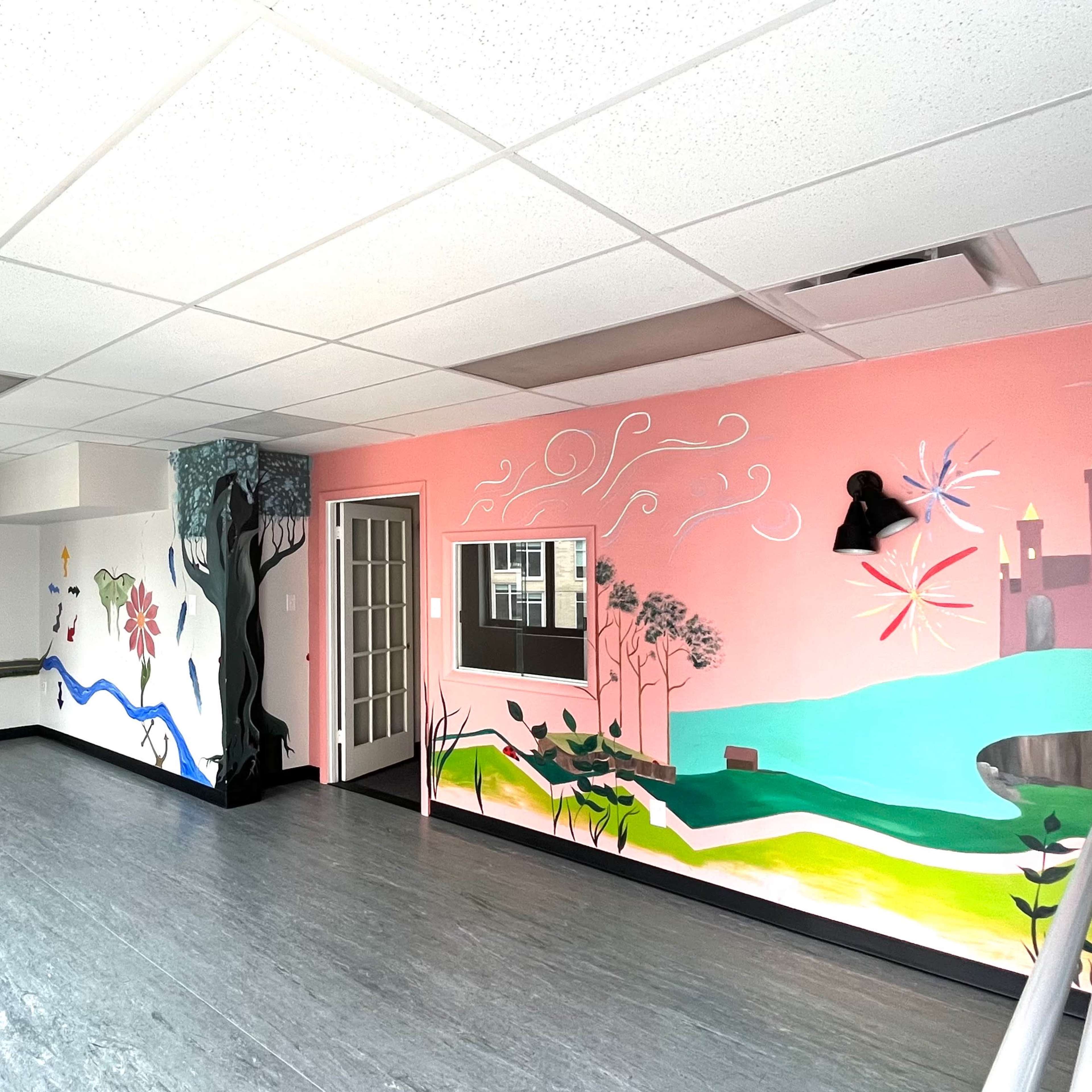 The room features colorful murals on the walls, a large open space with gray flooring, and windows allowing natural light.