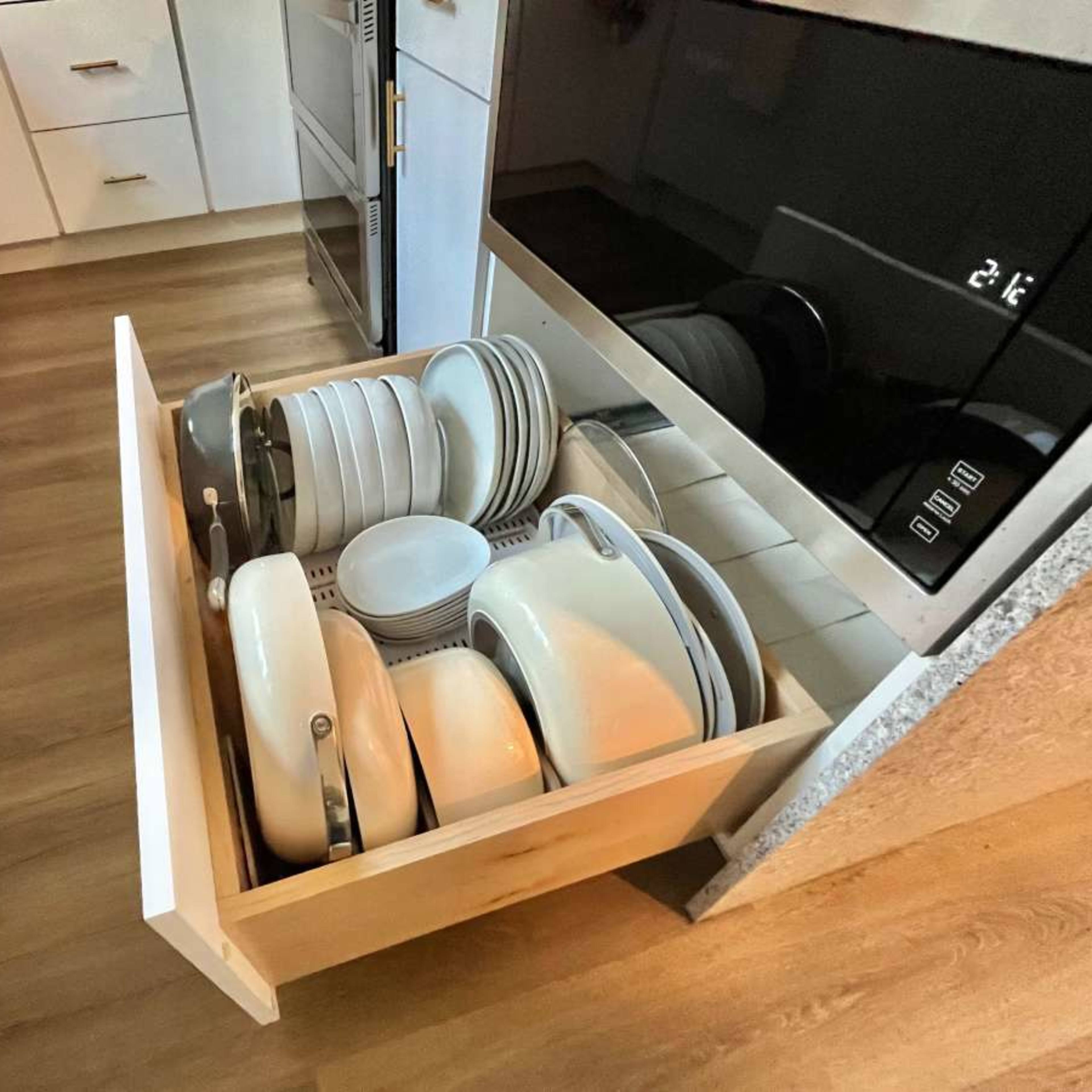 A kitchen drawer is open, containing neatly stacked plates, bowls, and cookware.