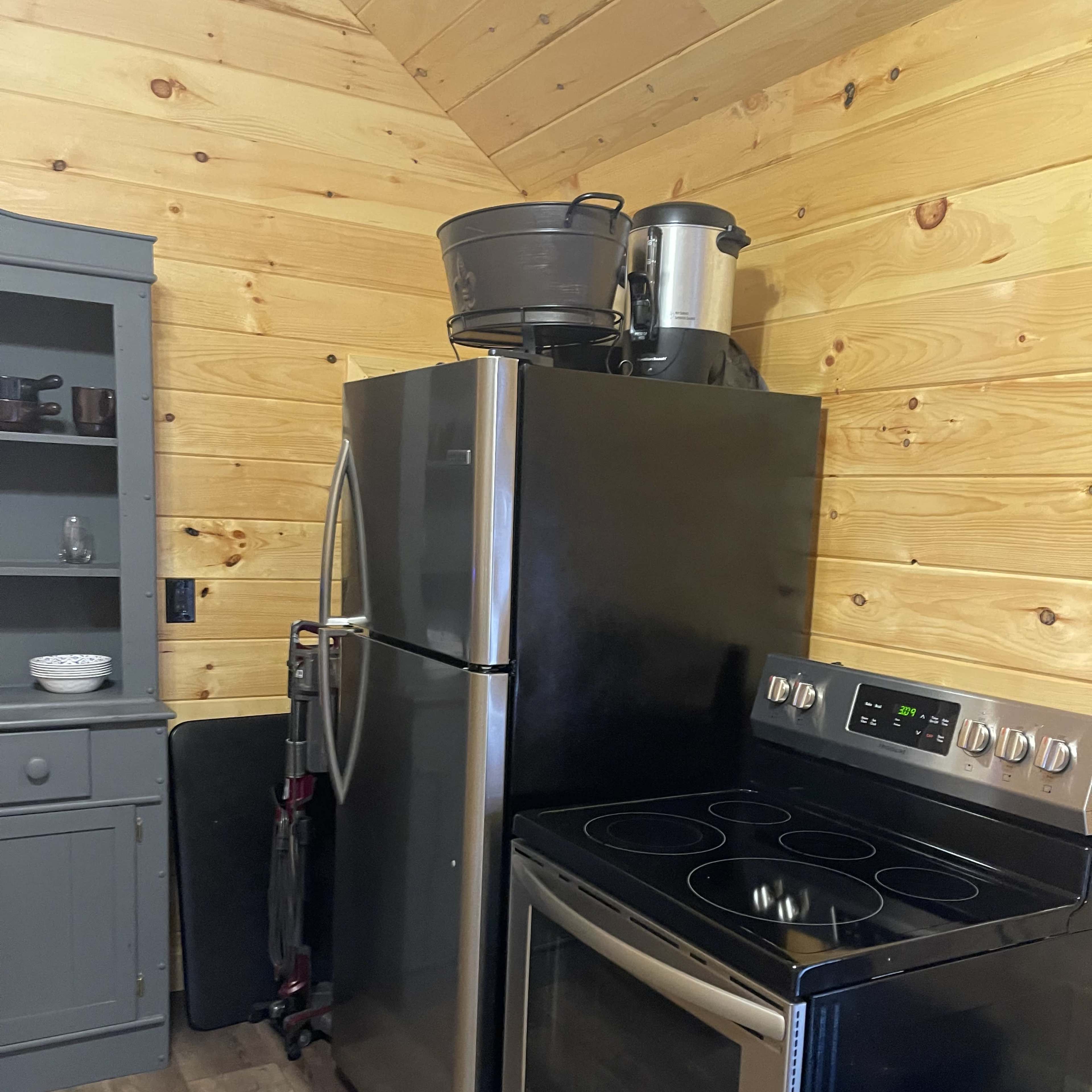 A kitchen area featuring a stainless steel refrigerator, a black electric stove, and wooden walls.