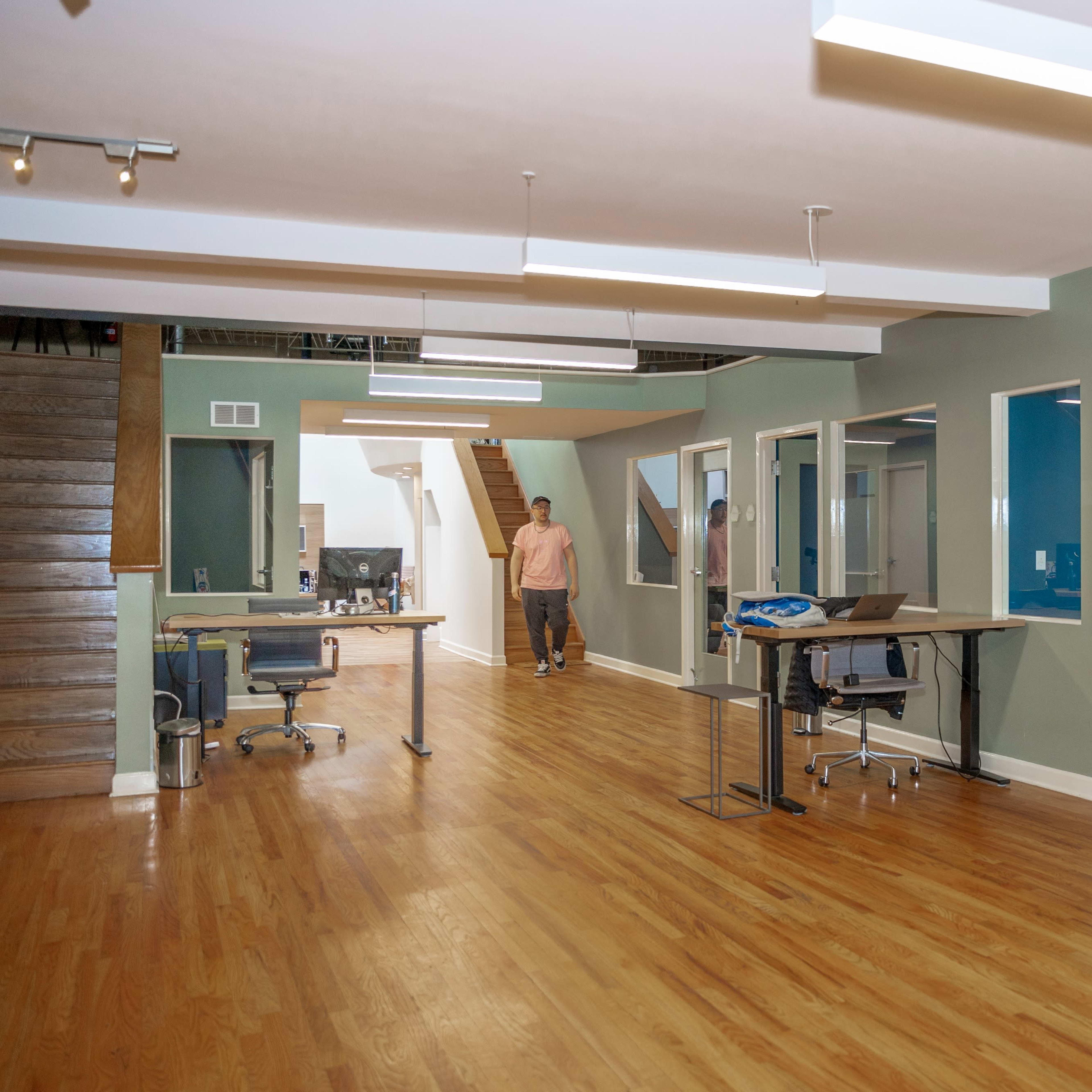 An office interior with wooden floors, green walls, and several desks arranged in an open layout.