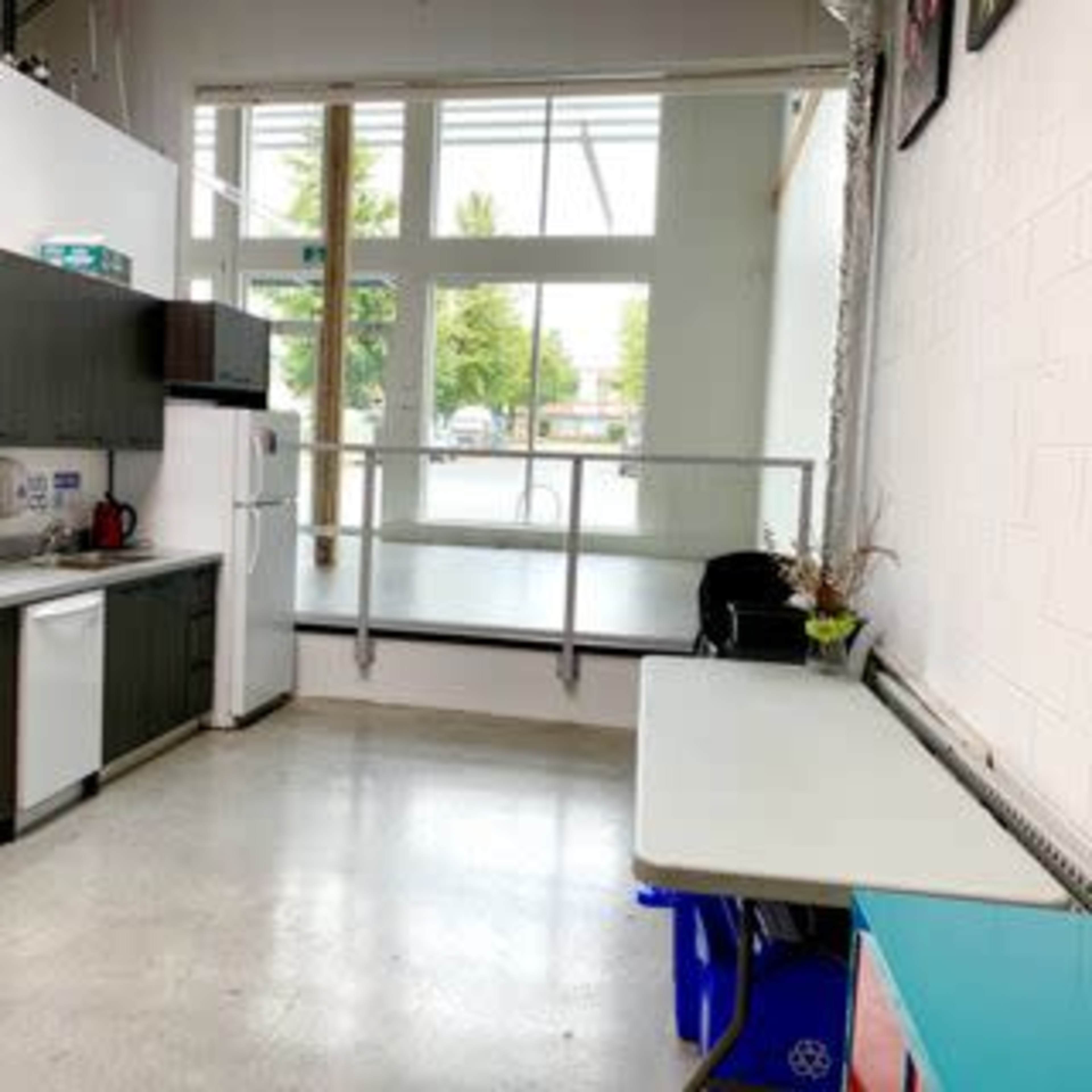 A kitchen area with dark cabinetry, a microwave, a refrigerator, and a table beside a large window that provides natural light.