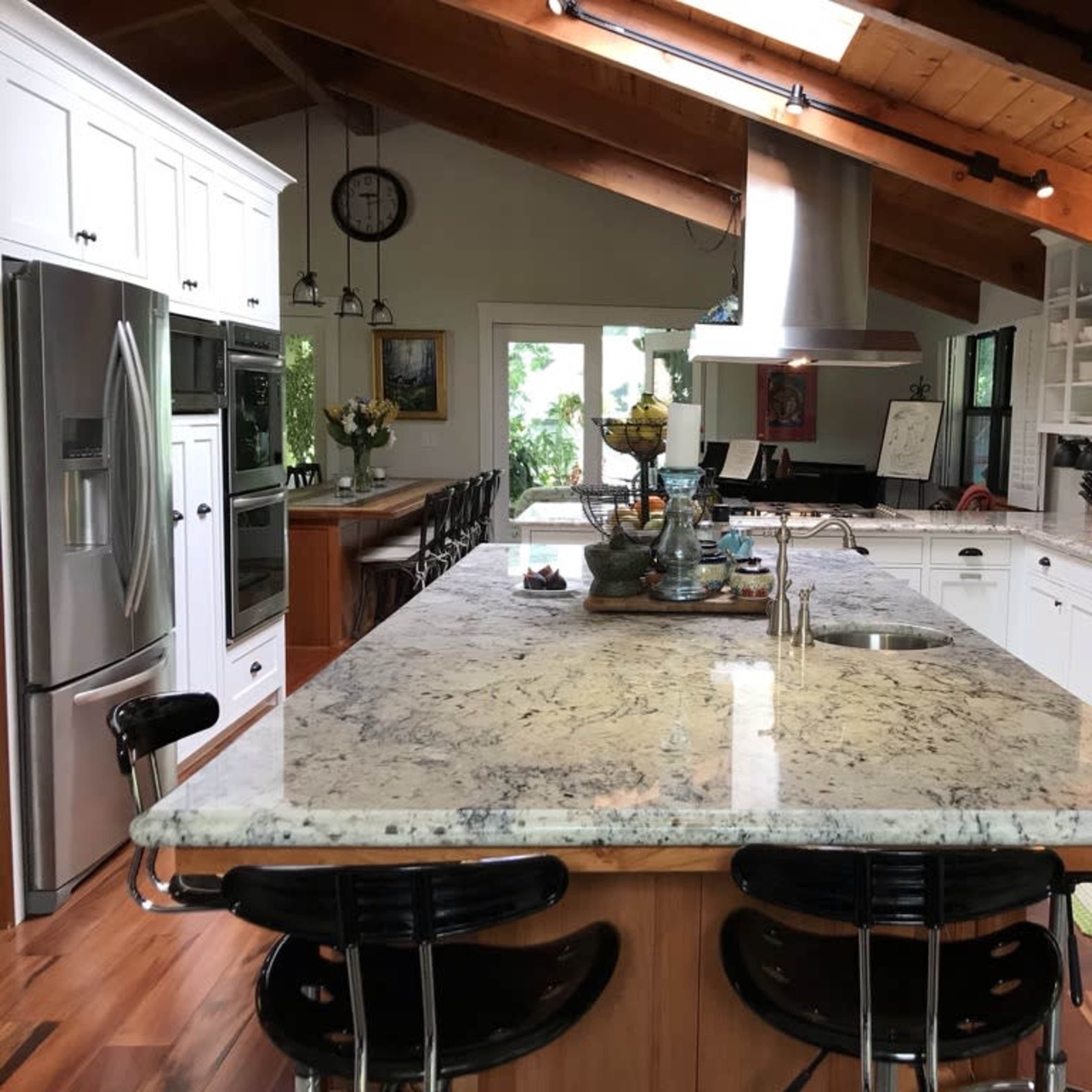 A spacious kitchen features a large granite island, modern appliances, and wooden beams on the ceiling.