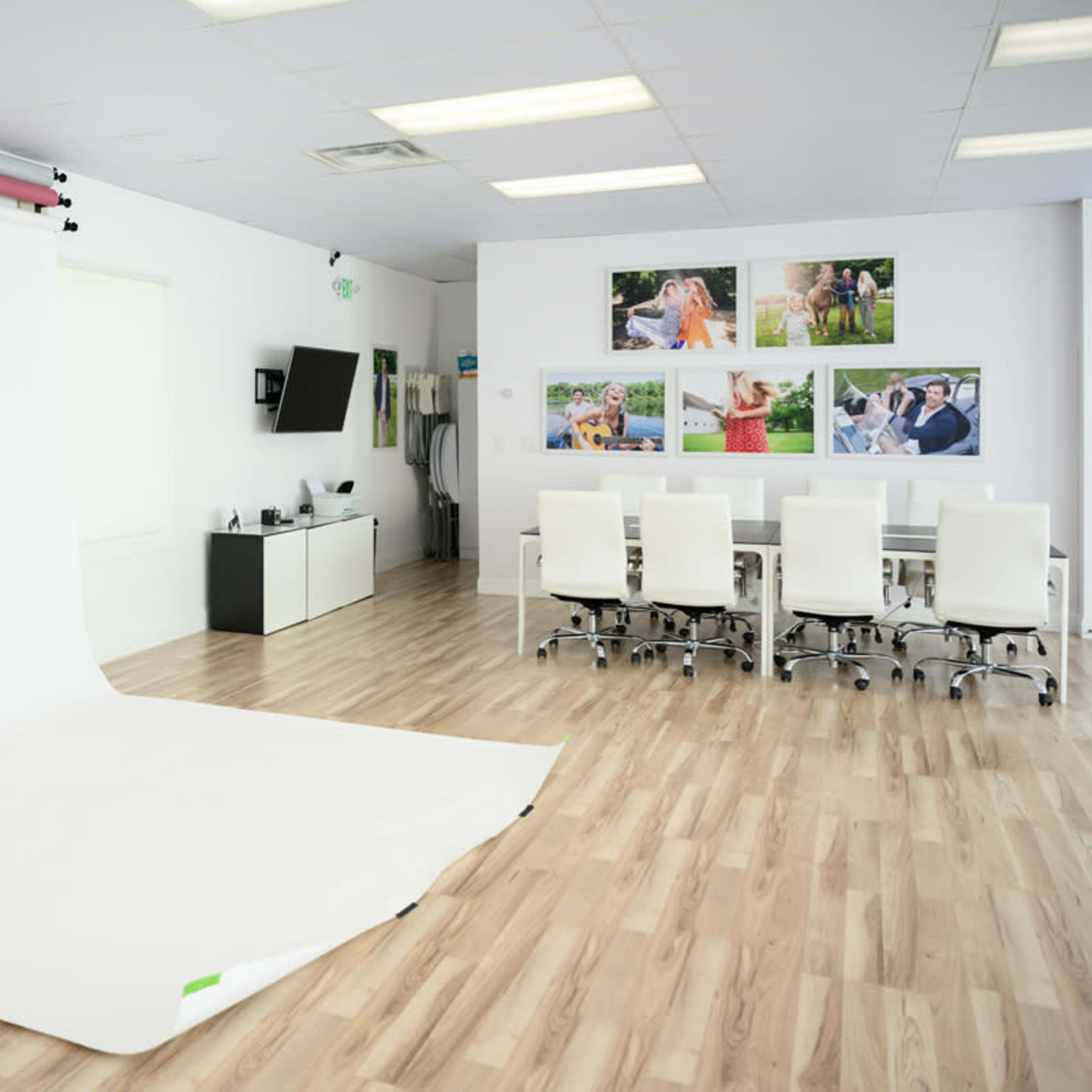 A photography studio with a white backdrop, a table surrounded by white chairs, and framed photographs on the wall.