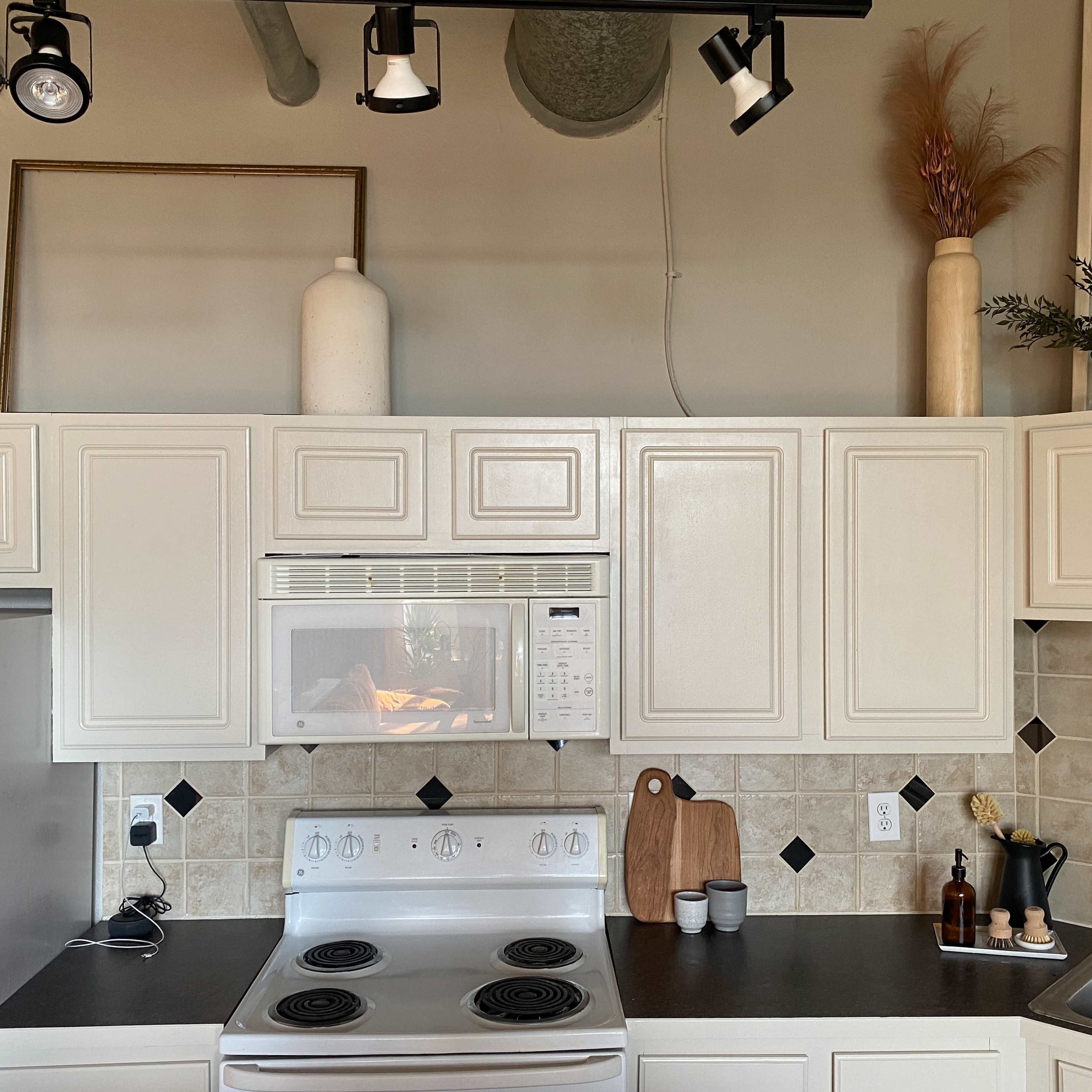 A kitchen with white cabinetry, a microwave, a stove, and a sink, featuring decorative items on the shelves above.