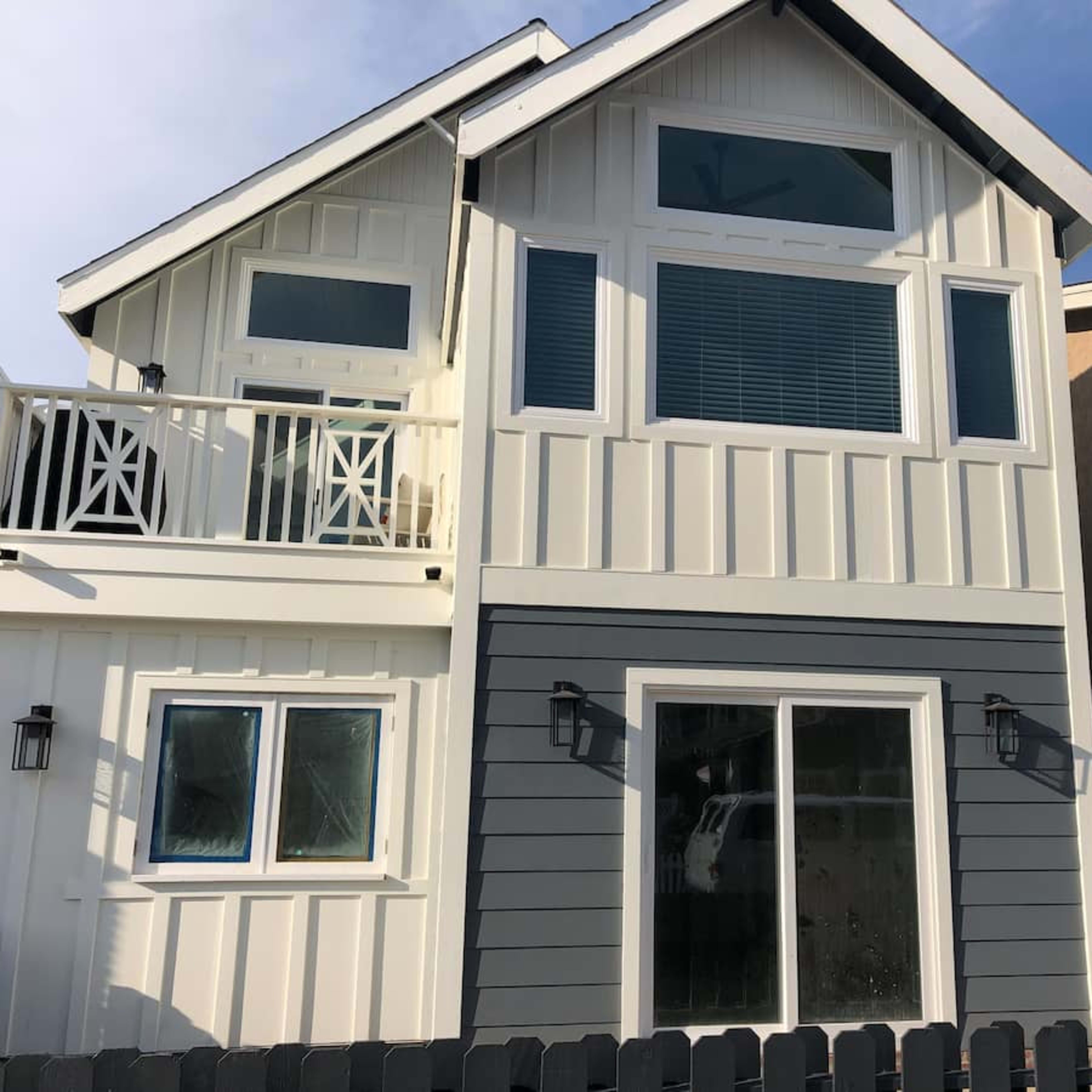 A two-story house with a mix of white and gray siding, large windows, and a front porch with a railing.