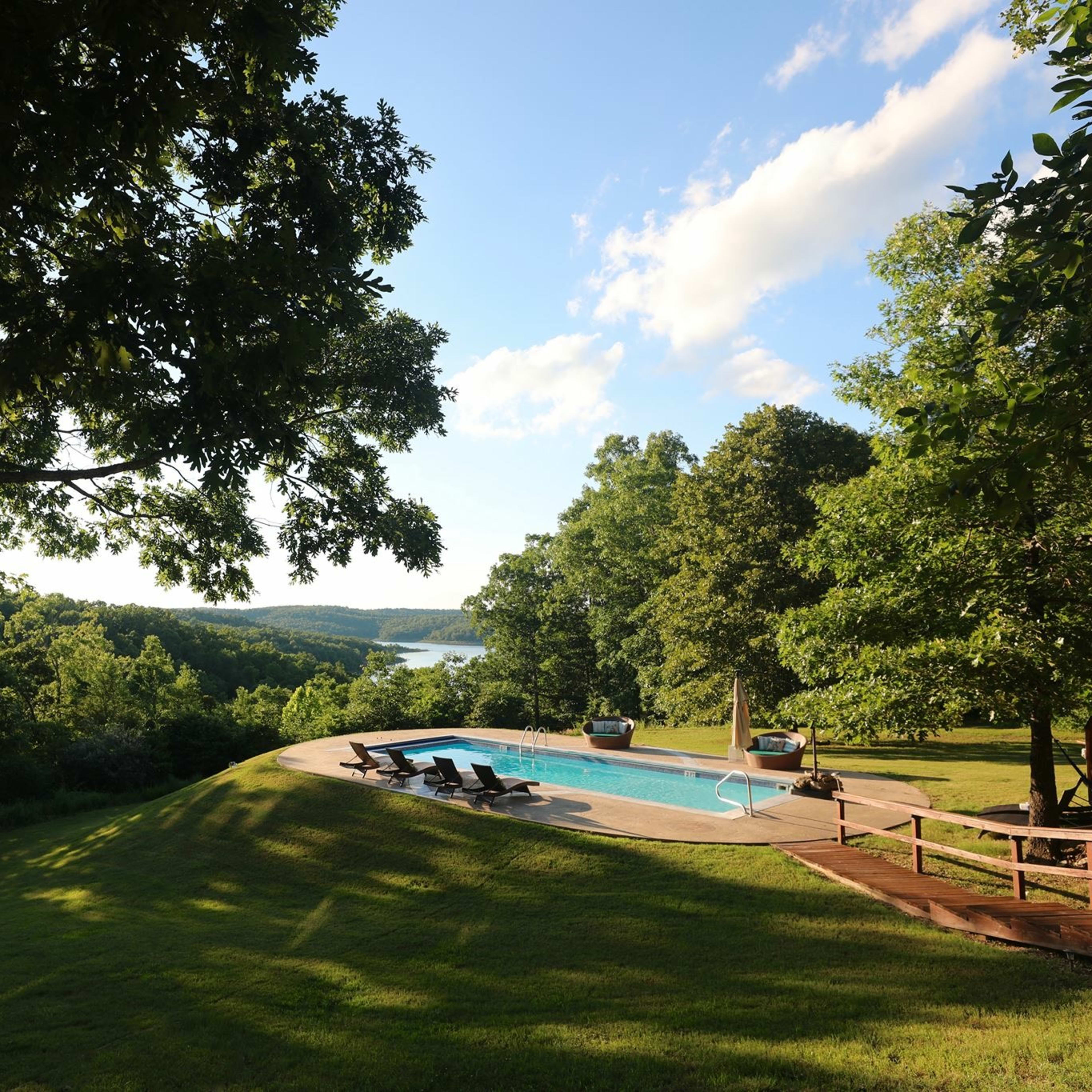 A swimming pool is situated on a lawn overlooking a valley with trees and a body of water in the distance.
