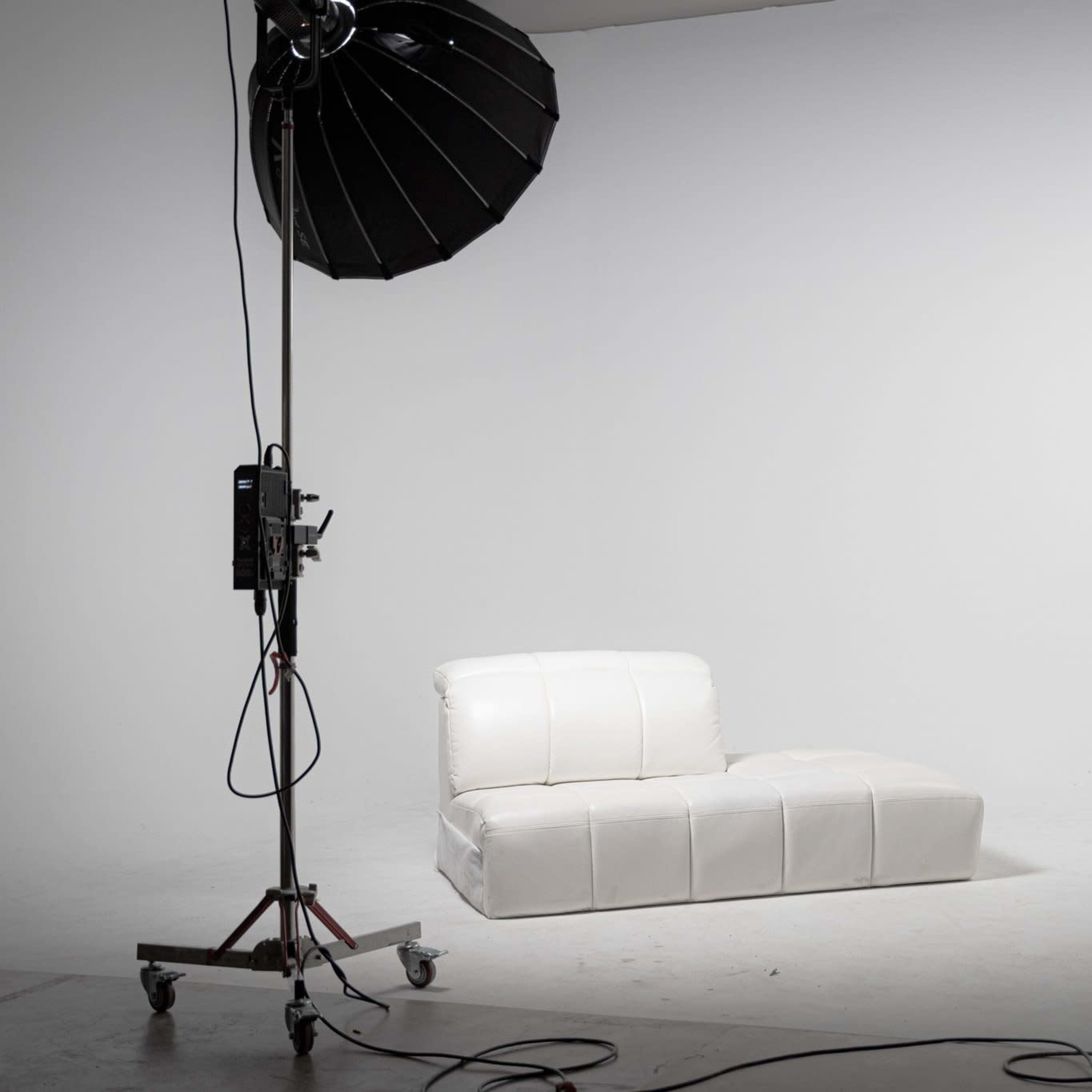 A white sofa is positioned between two studio lights in a minimalist photography studio.