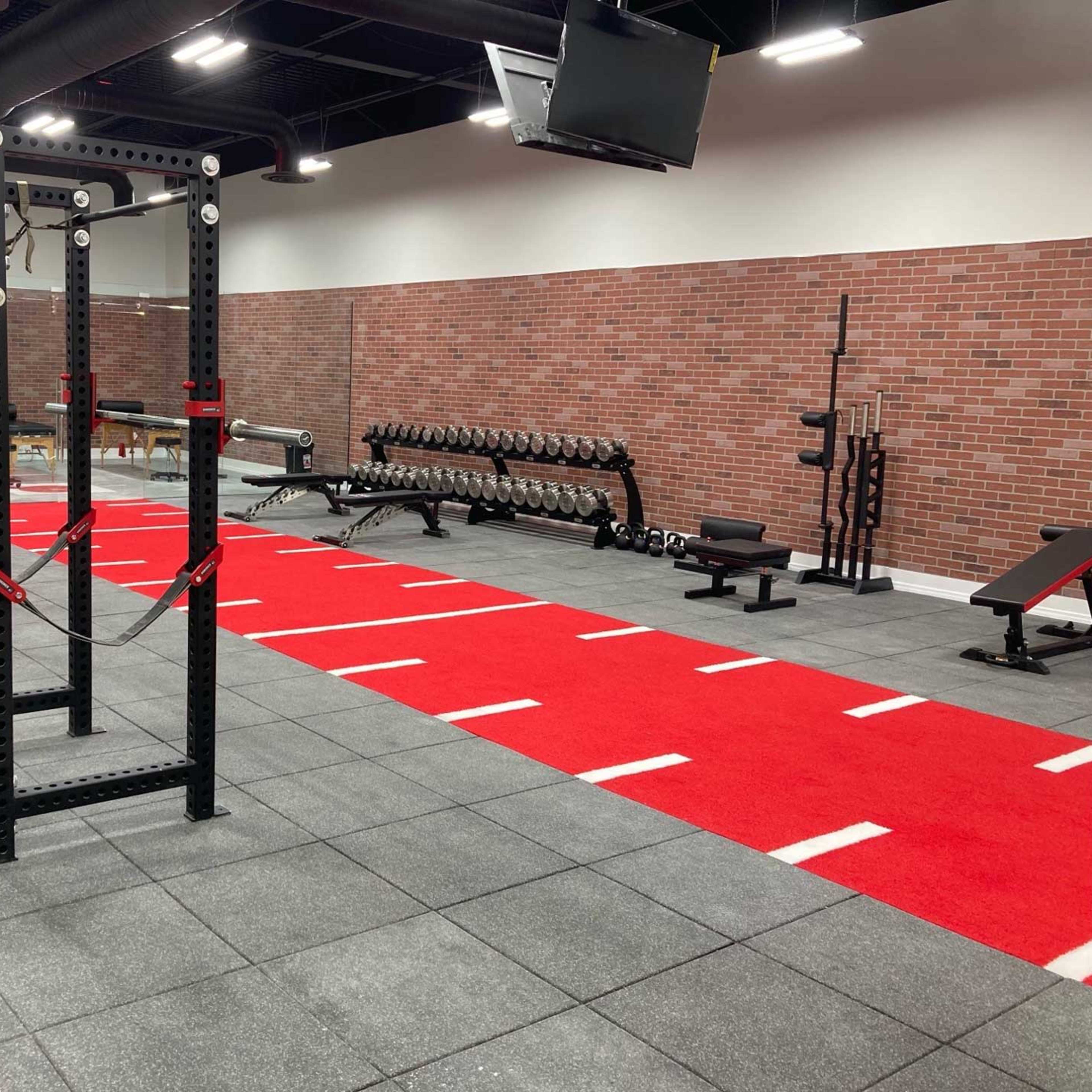 A well-equipped gym featuring weightlifting equipment, a red running track, and a brick wall backdrop.