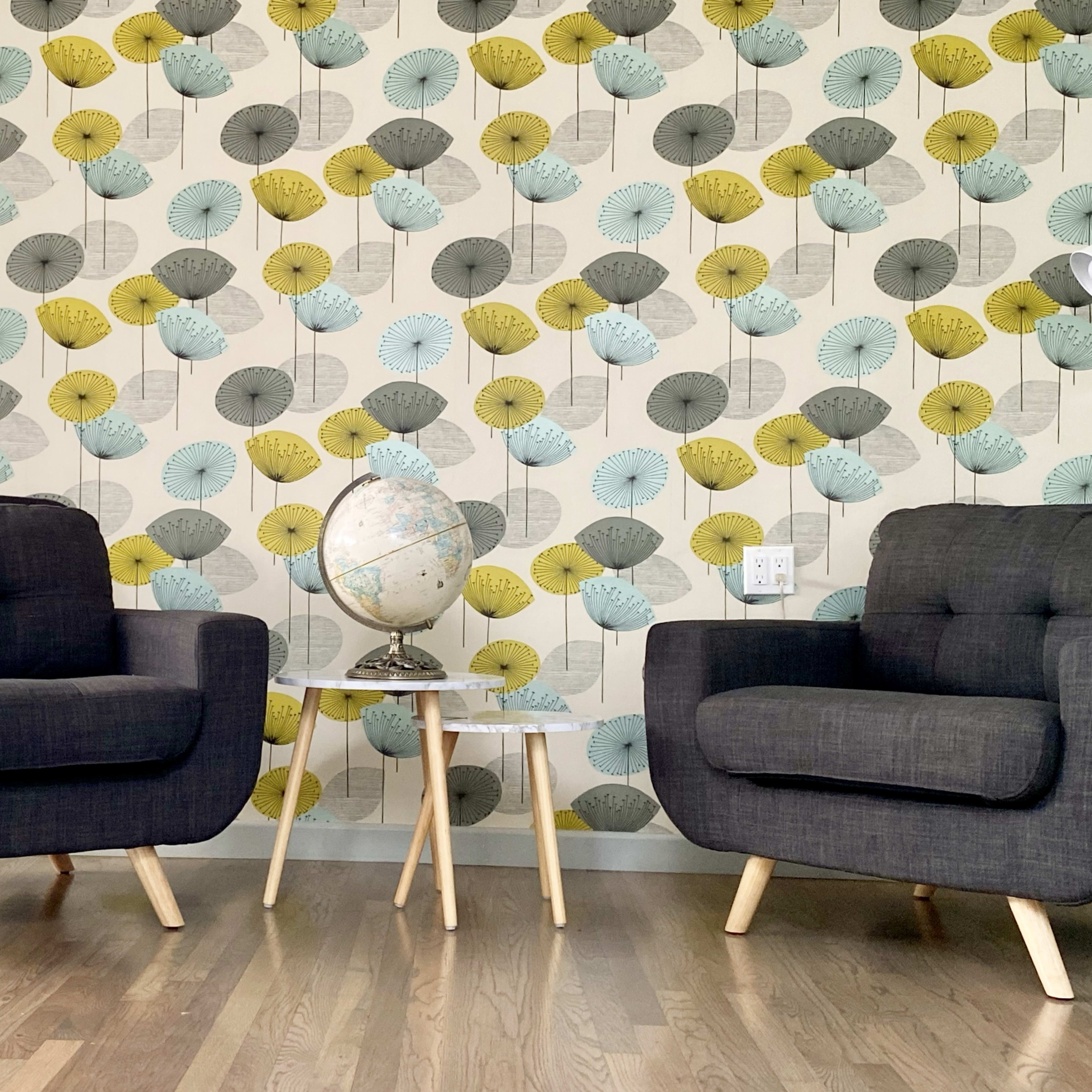 Two dark-colored armchairs sit opposite each other in a room with a patterned floral wallpaper, accompanied by a small side table holding a globe.