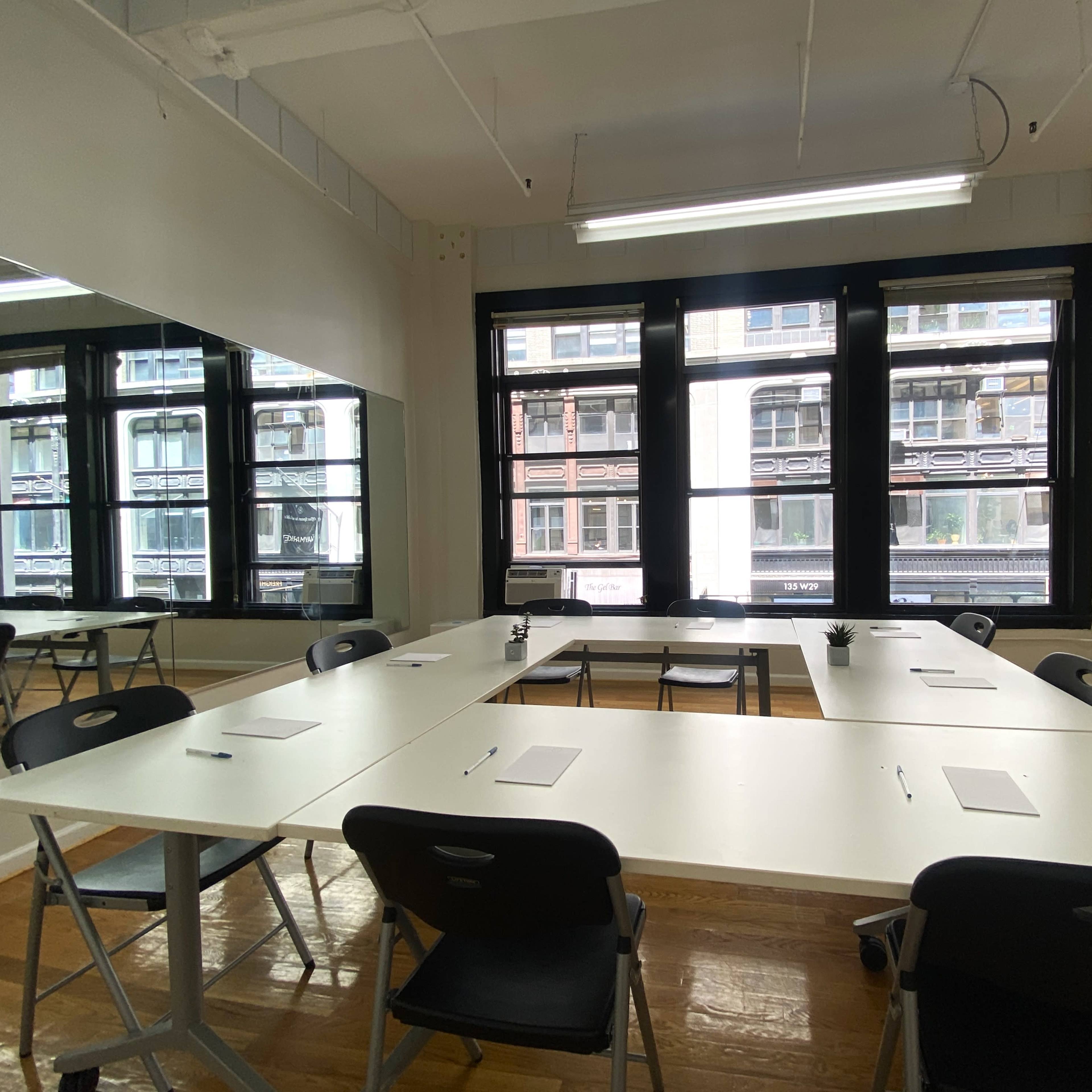 A conference room features a large rectangular table surrounded by black chairs, with several notepads placed on the table and large windows providing natural light.