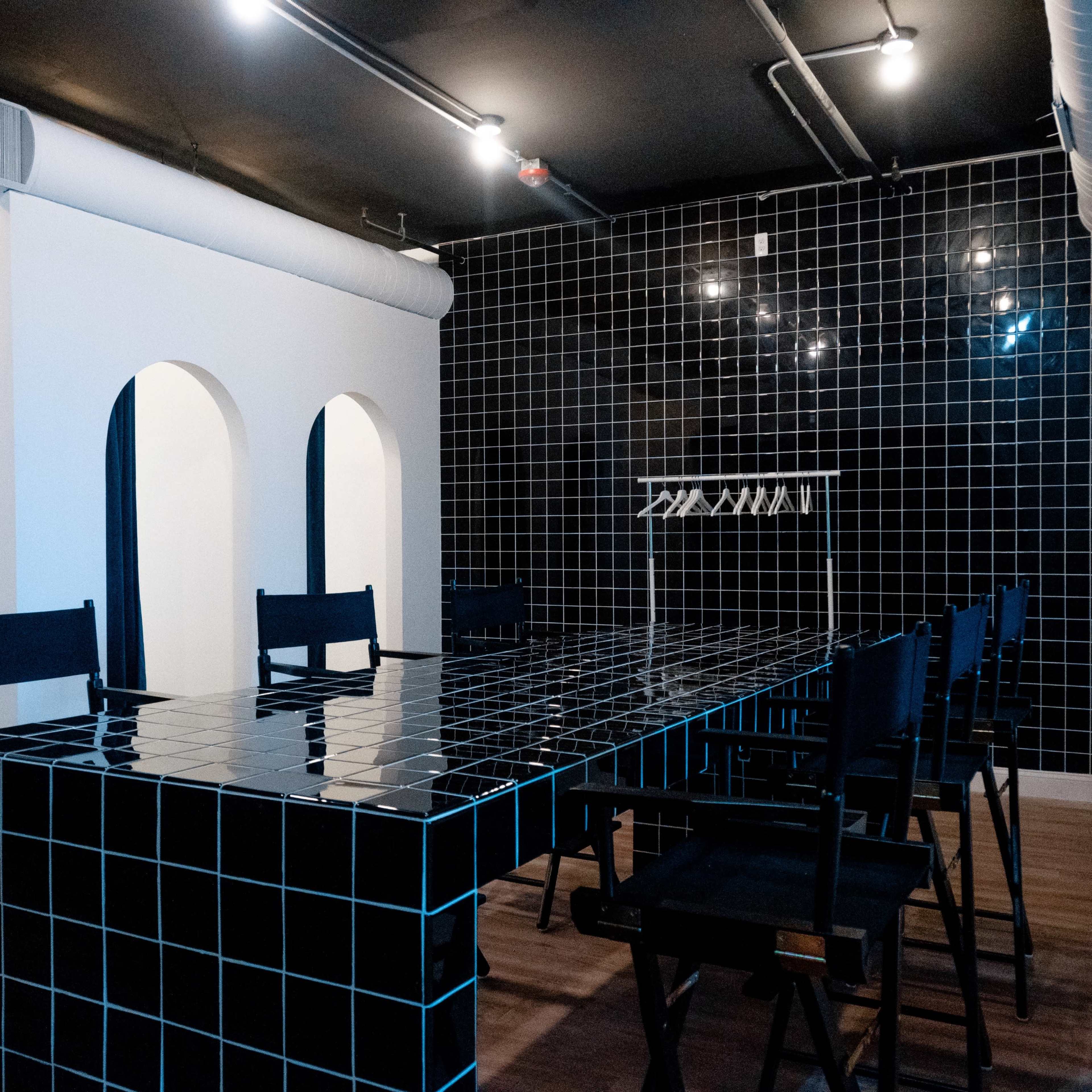 A modern meeting room featuring a large black tiled table surrounded by black chairs, with a black tiled wall and arched openings on one side.