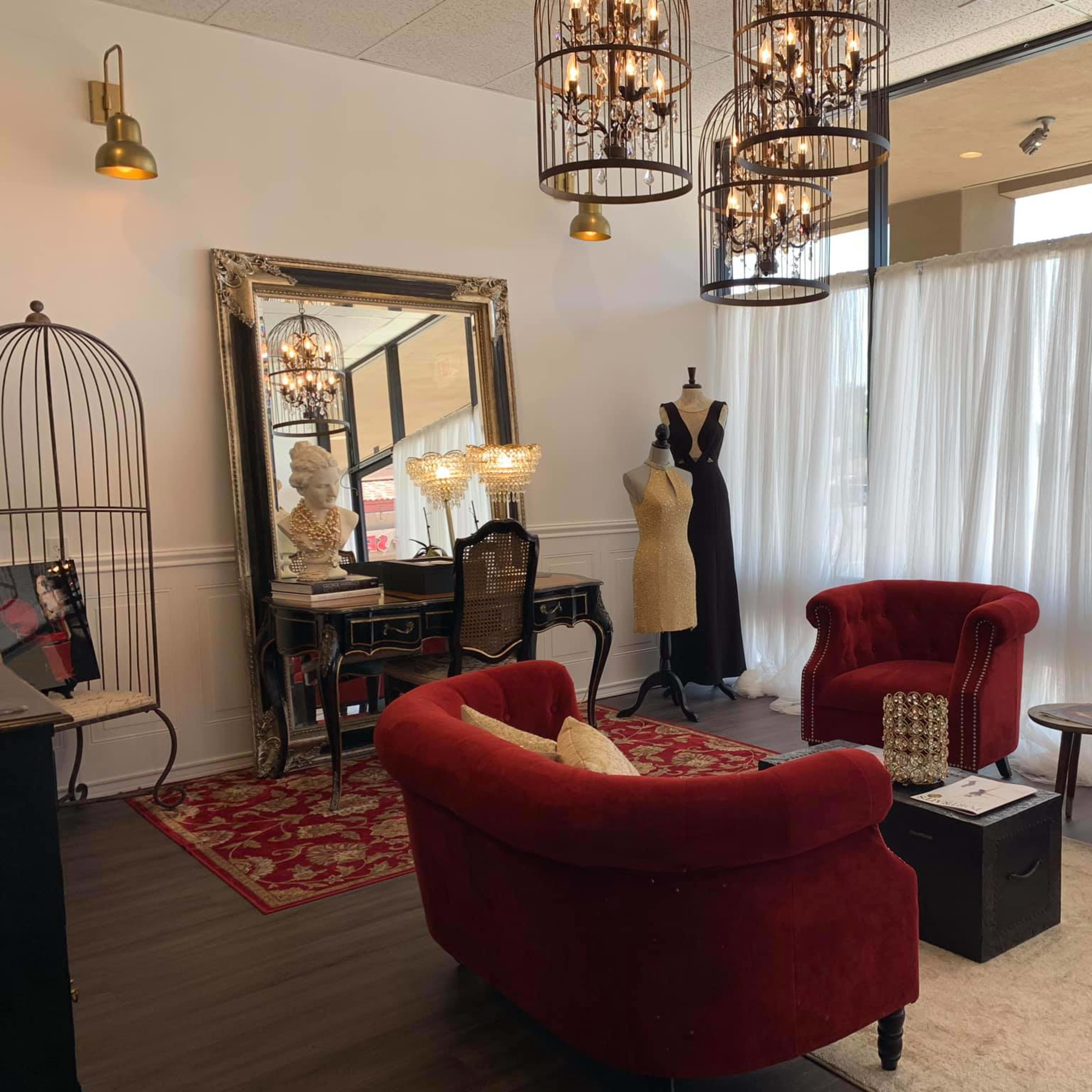 A stylish boutique interior featuring red velvet chairs, a mirror, a mannequin, a dressing table, and draped curtains.