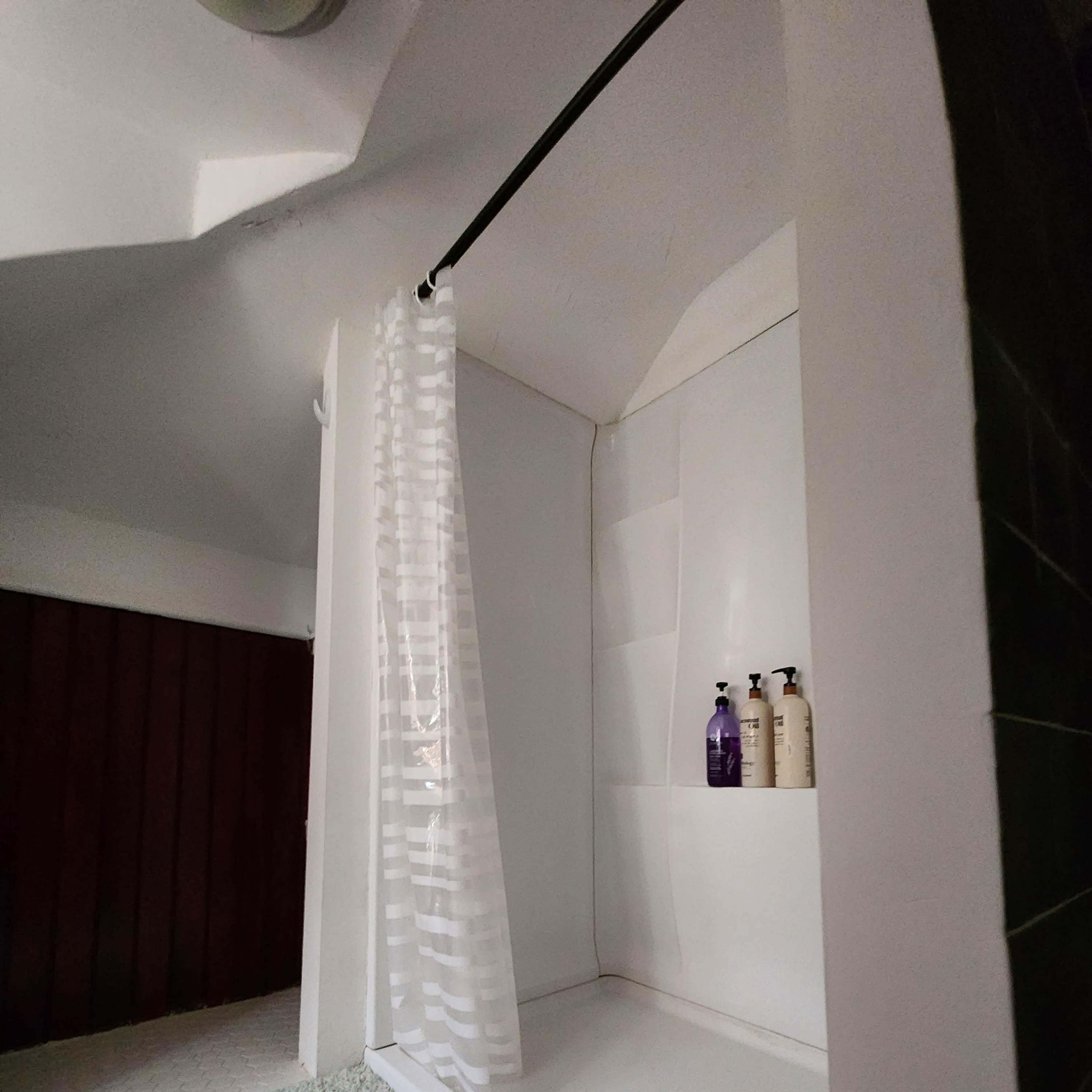 A simple shower area with a white curtain, a shower stall, and several bottles placed on a shelf.