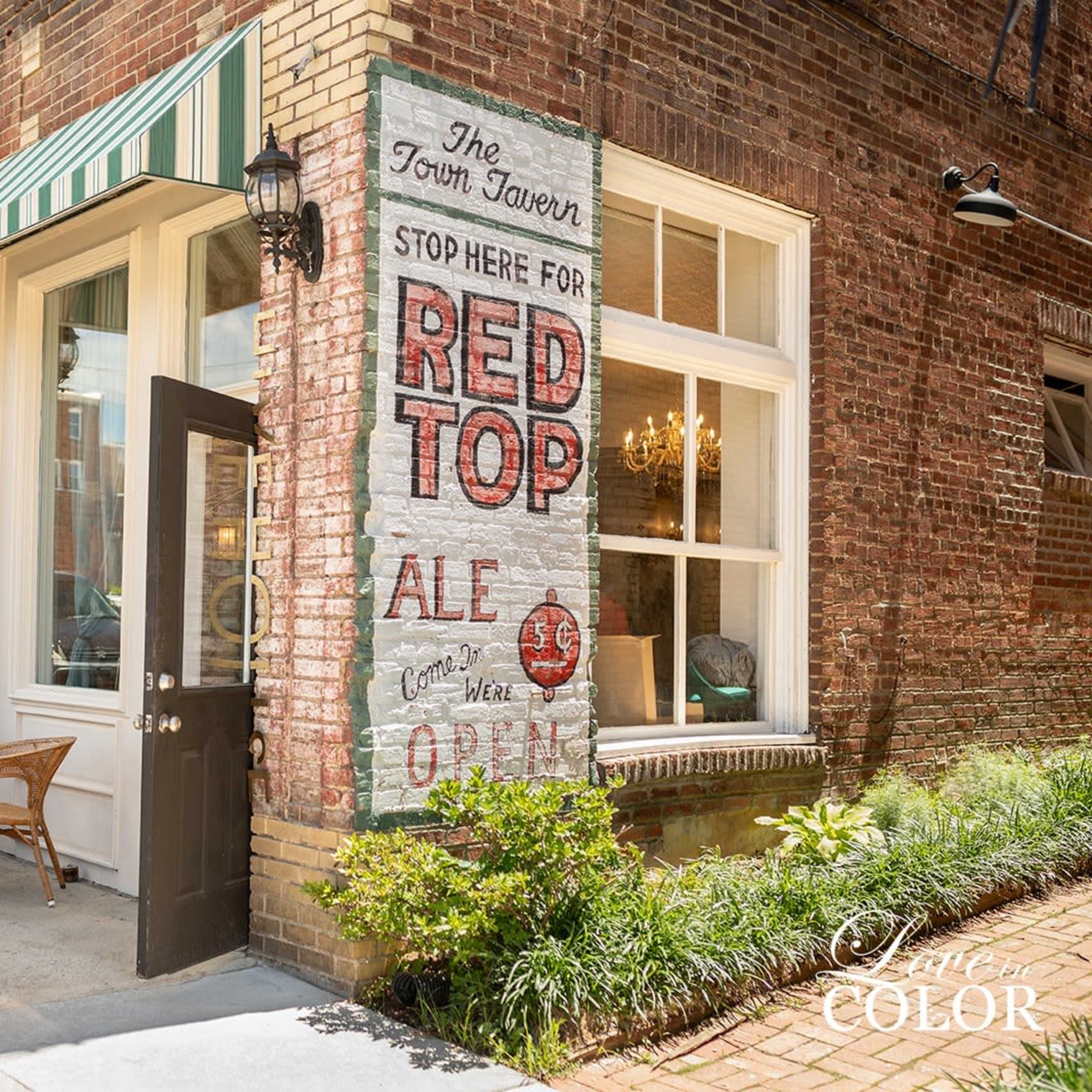 The exterior of a brick building with a painted sign advertising "Red Top Ale" and a door beneath a striped awning.