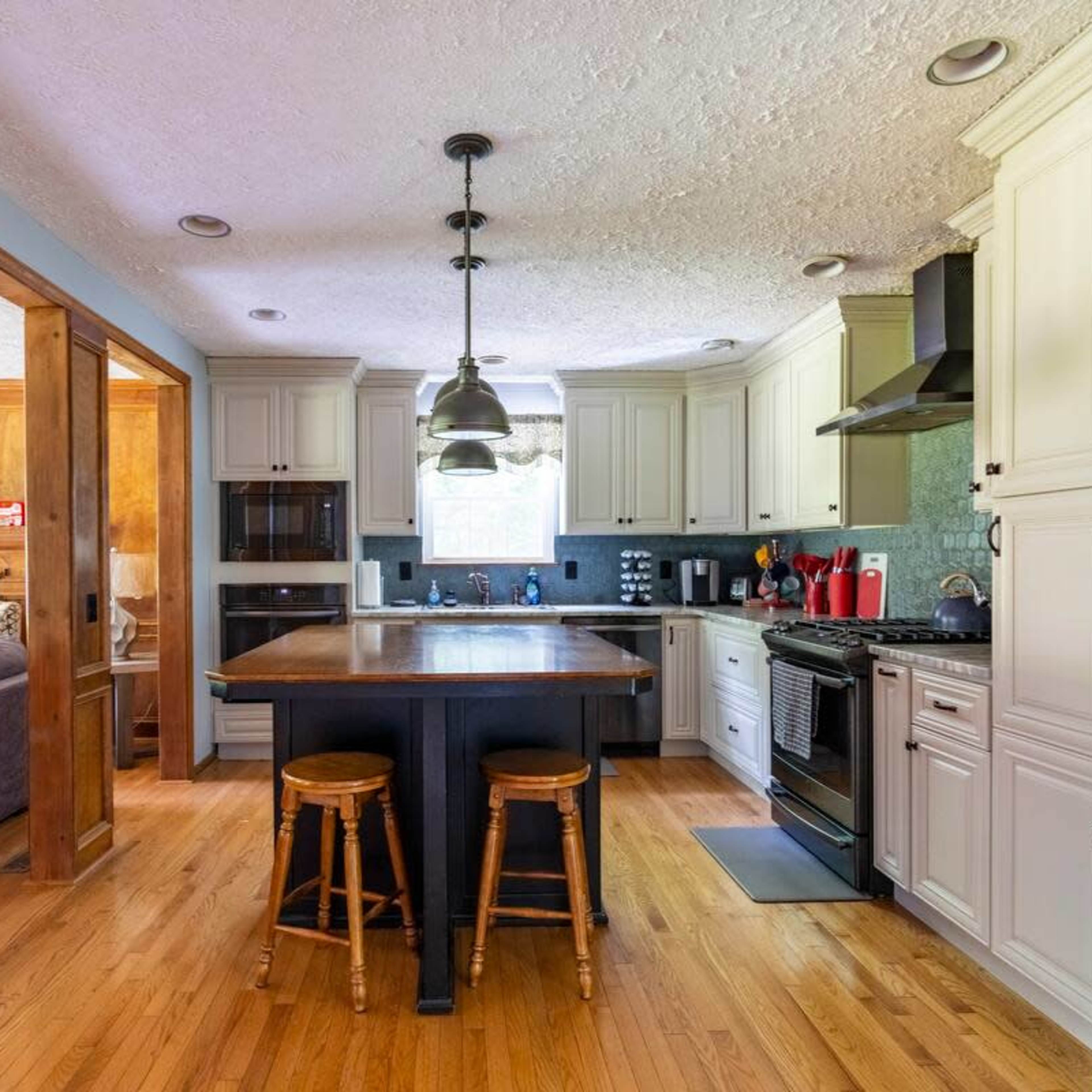 A modern kitchen features white cabinetry, a central island with two stools, and stainless steel appliances.