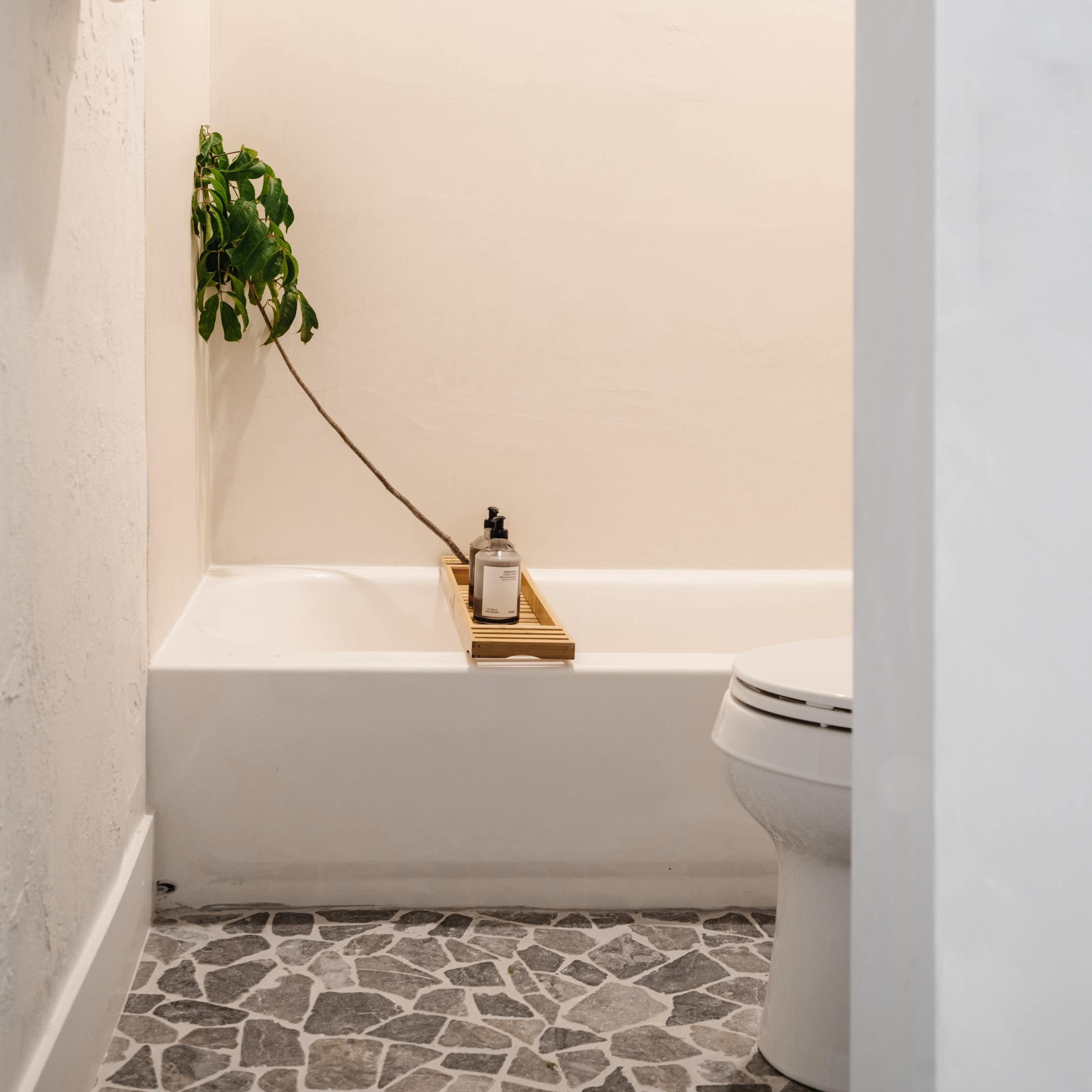 A small bathroom with a bathtub, a toilet, a wooden tray holding a candle, and a towel rack with rolled towels.