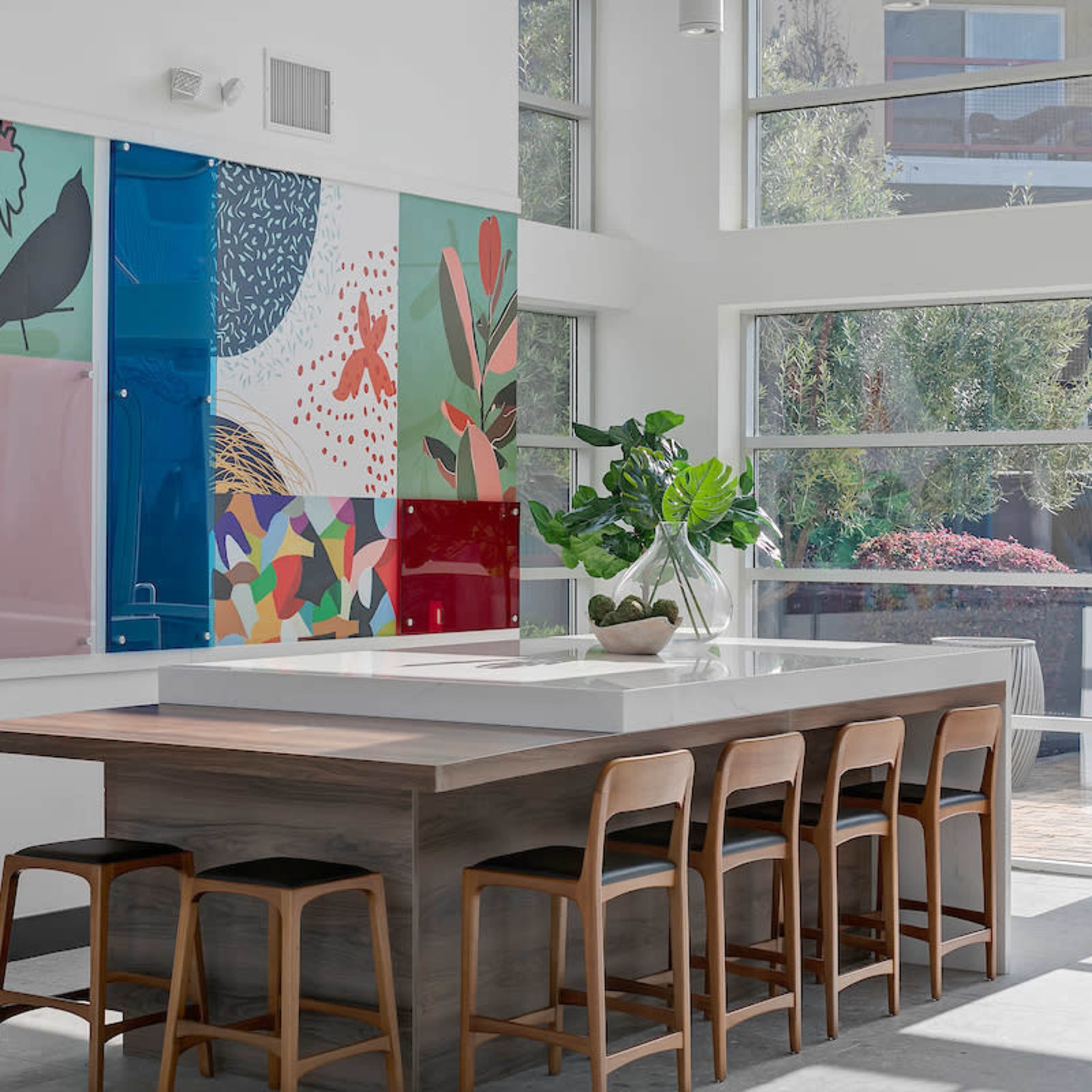 A modern kitchen features a large central island with wooden stools and a vibrant, abstract mural on the wall.