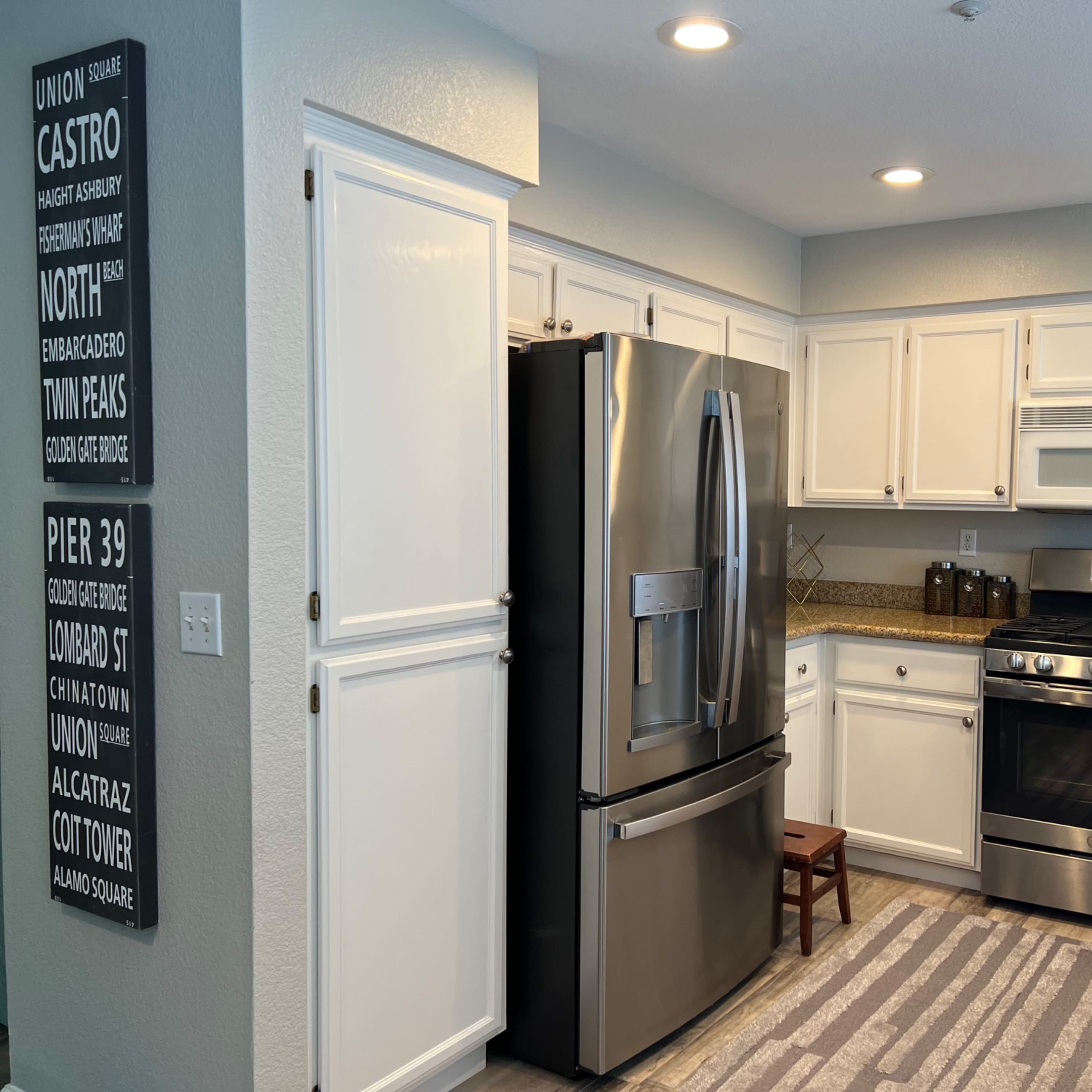 A modern kitchen with white cabinets, stainless steel appliances, and a gray patterned rug.