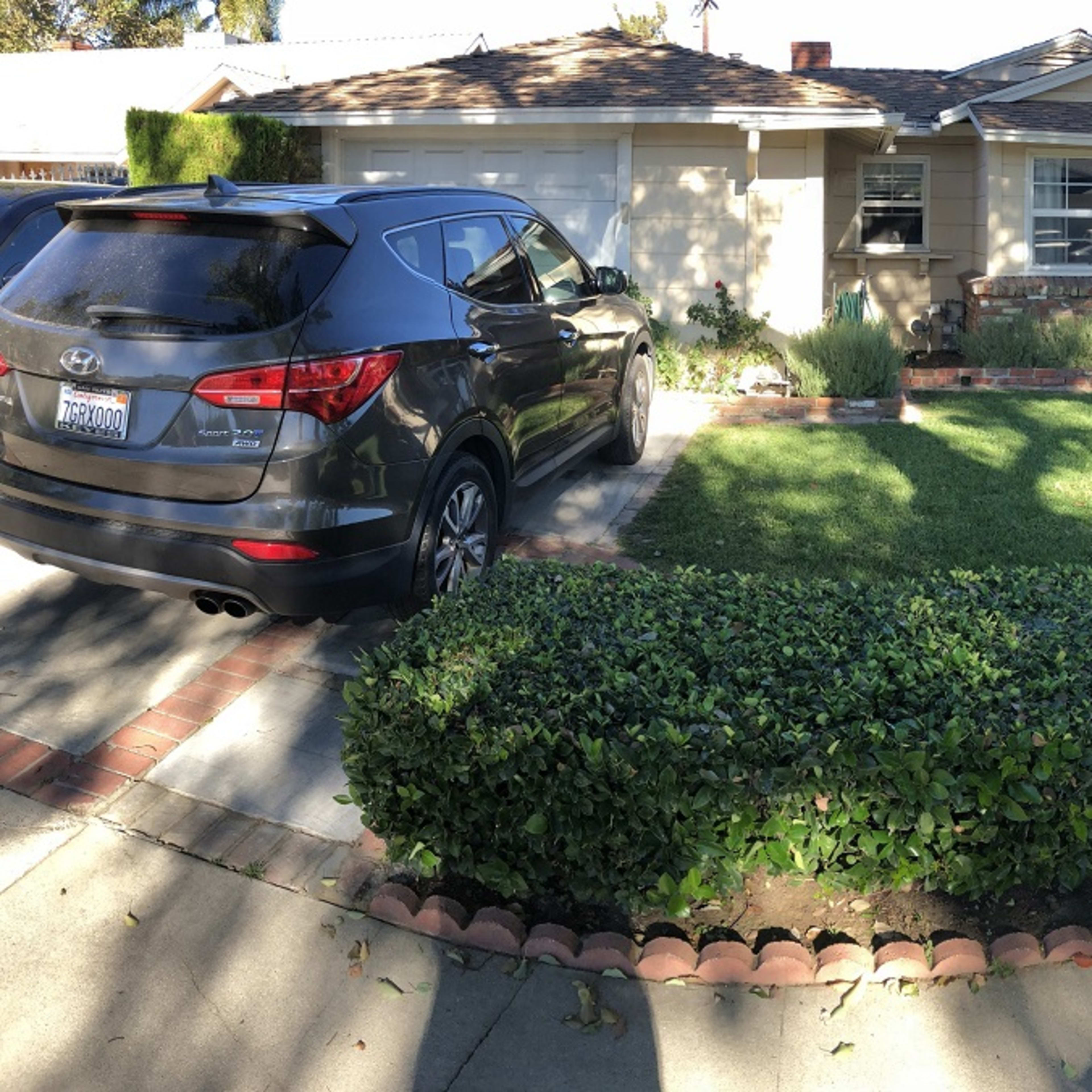 A black SUV is parked in the driveway of a single-story house with a neatly trimmed front lawn and hedges.