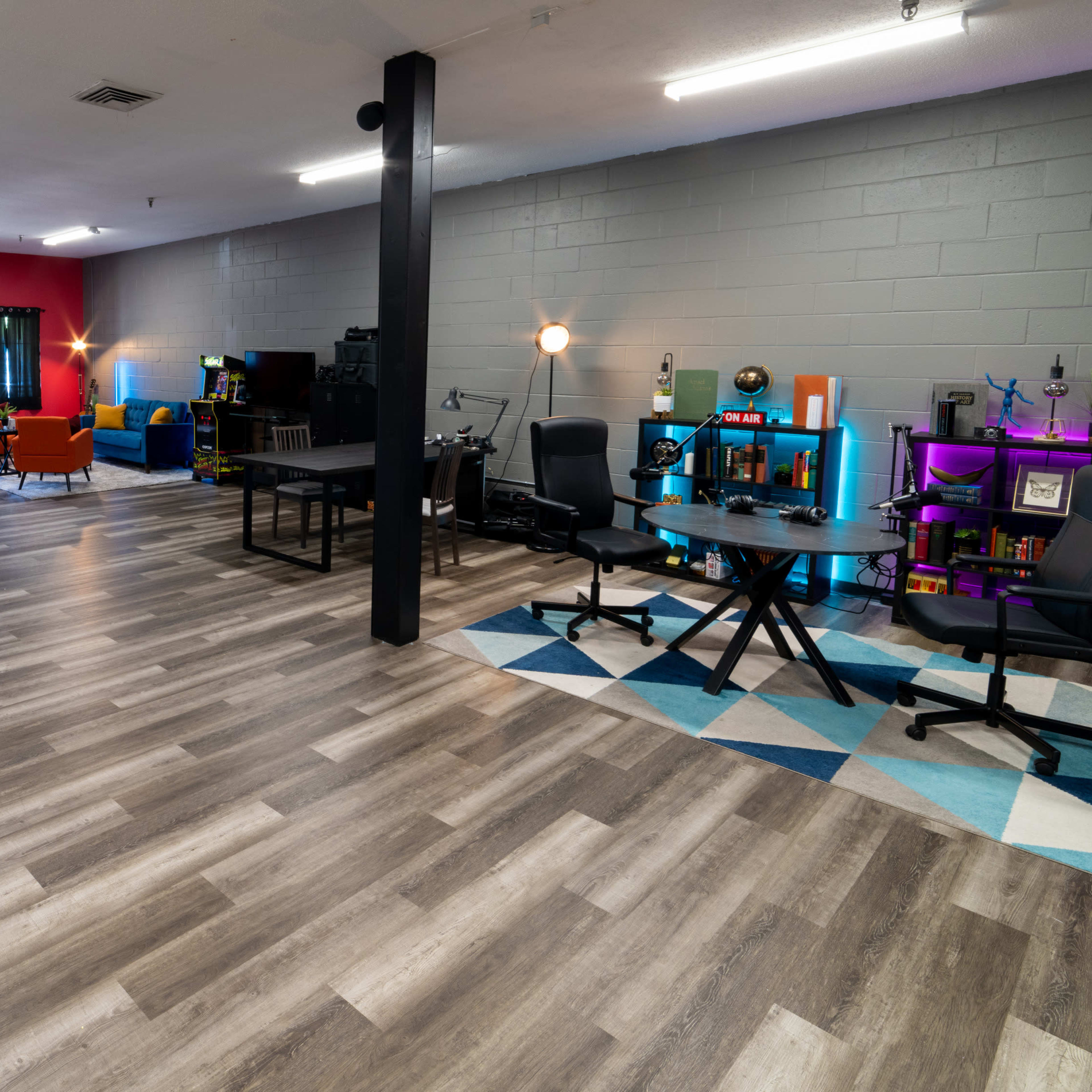A spacious room with a hardwood floor, featuring various workstations and colorful seating areas against a backdrop of gray walls and red accents.
