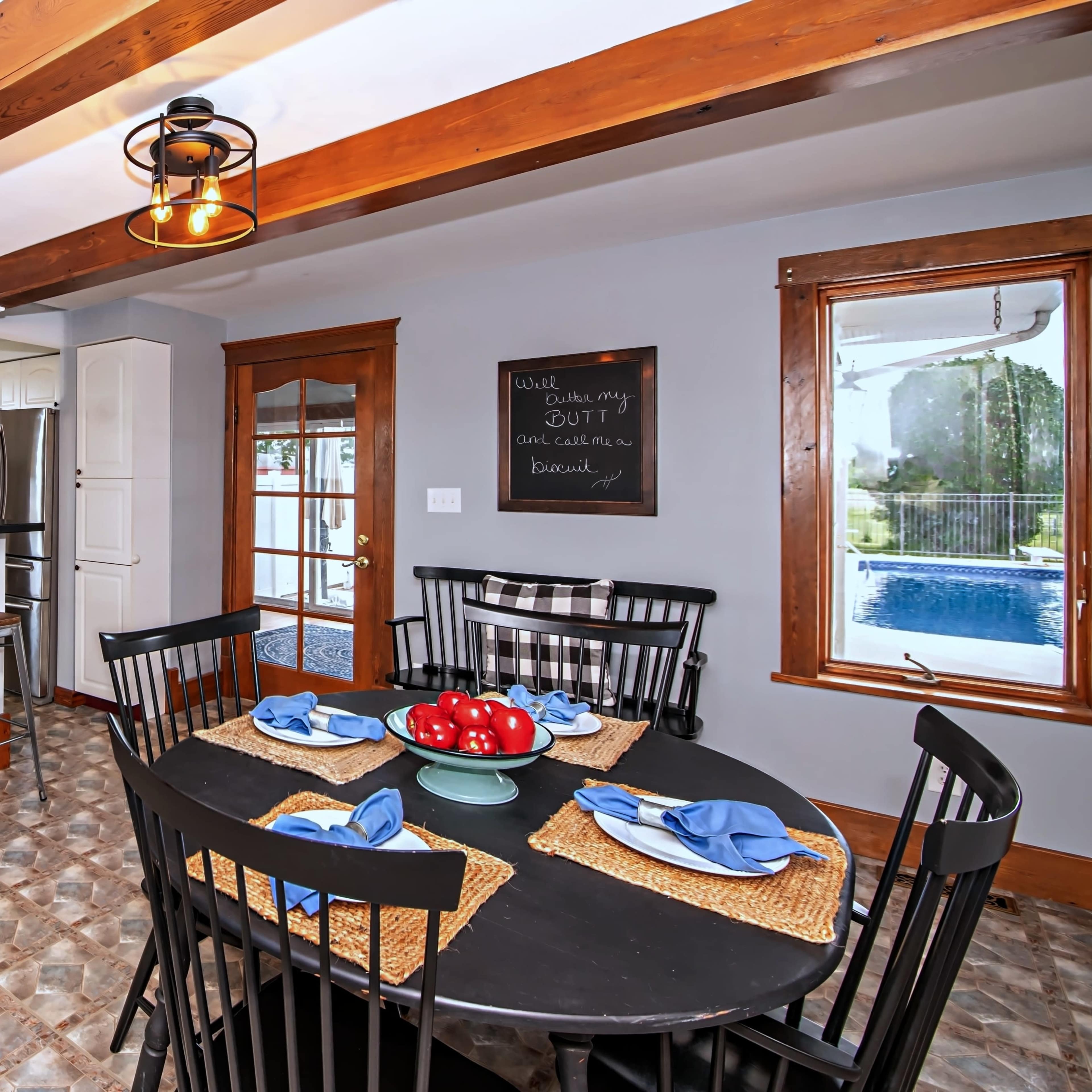 A modern kitchen features a dining area with a black table, bar seating, and a view of a pool outside.