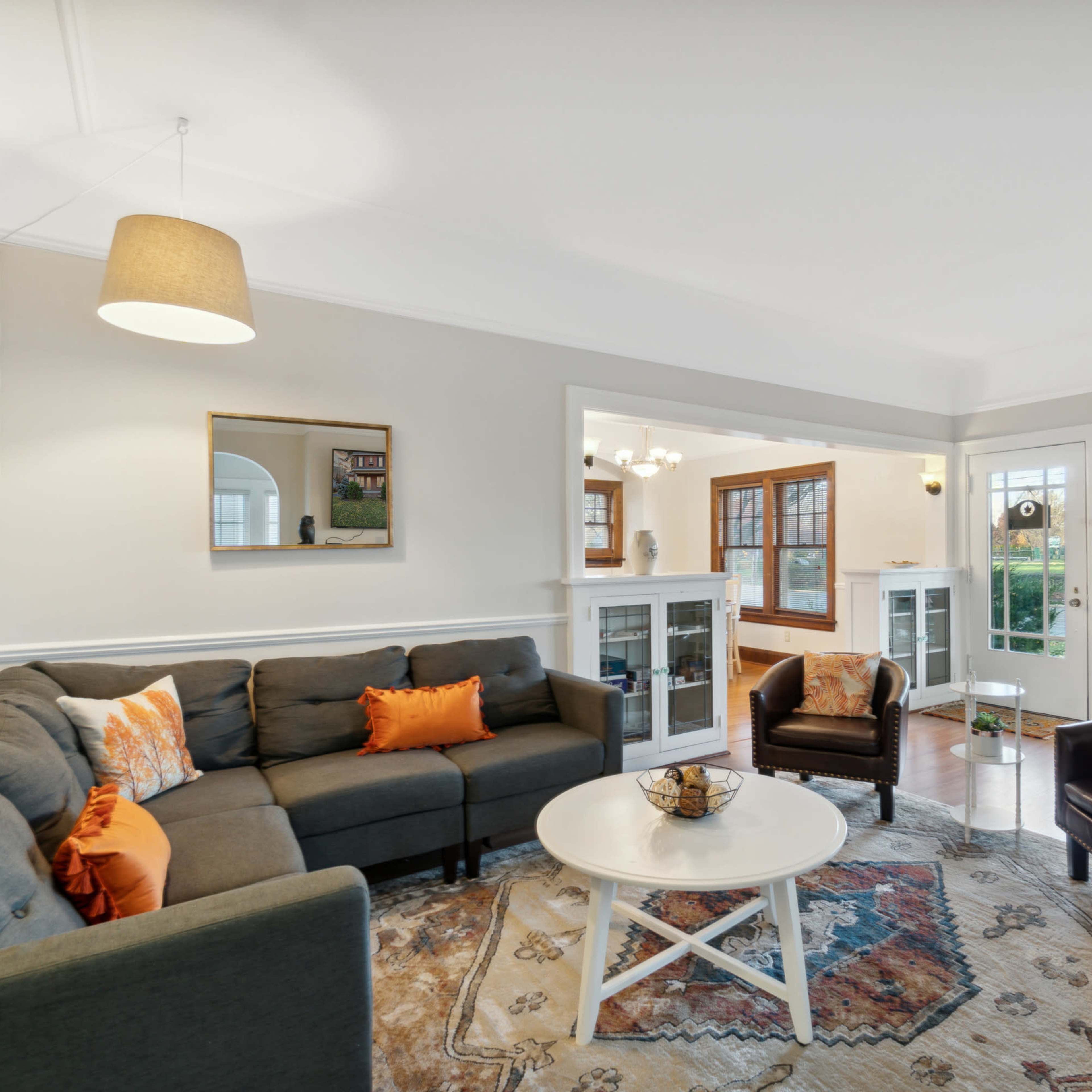 A living room with a gray sectional sofa, a round white coffee table, and large windows allowing natural light to illuminate the space.